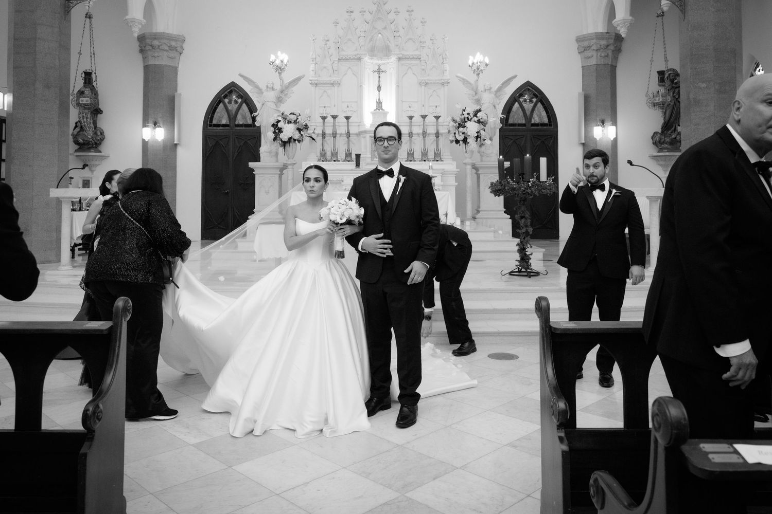 A black and white wedding ceremony photo showing guests and a dramatic cathedral setting.