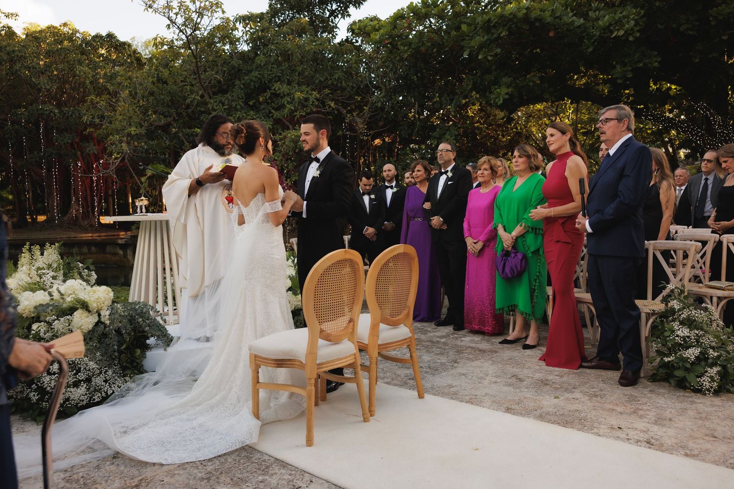 Garden wedding ceremony setup with chairs arranged outdoors and colorfully dressed guests in attendance.