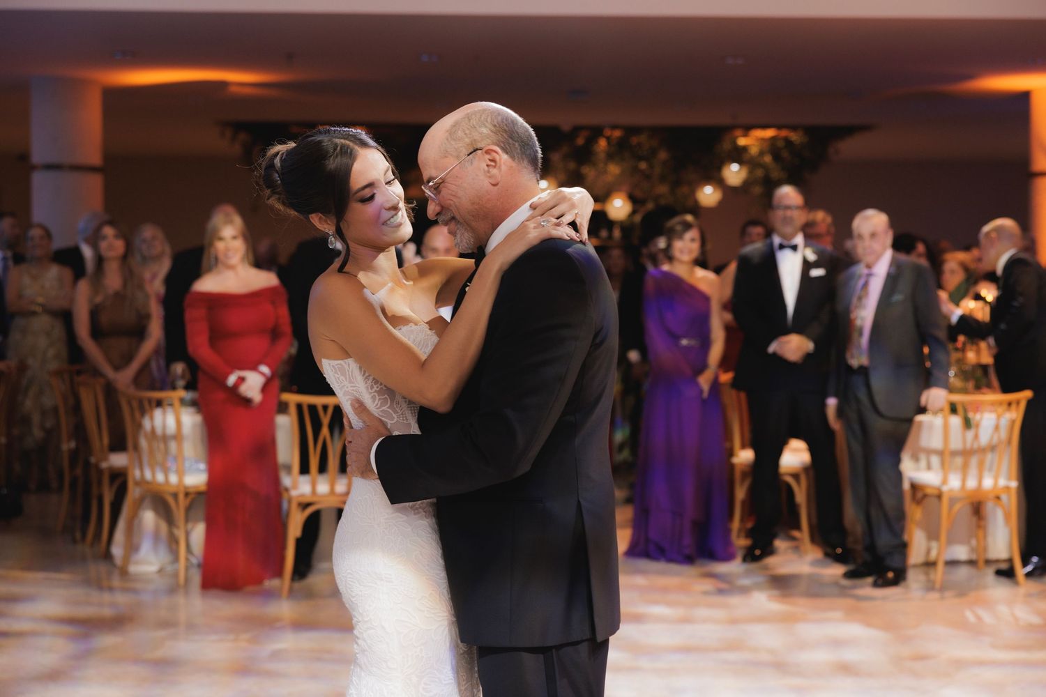 A wedding couple shares an intimate dance surrounded by guests in a beautifully decorated reception venue.
