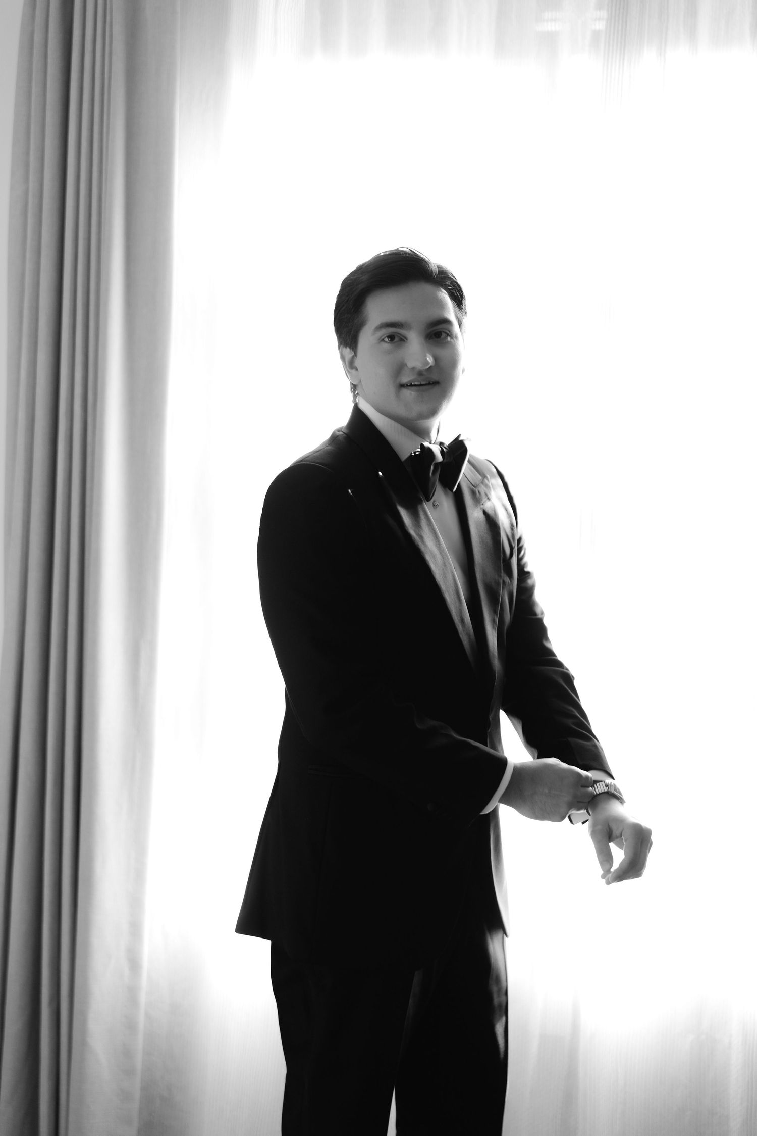 Black and white portrait of person adjusting sleeve cuff in formal attire.