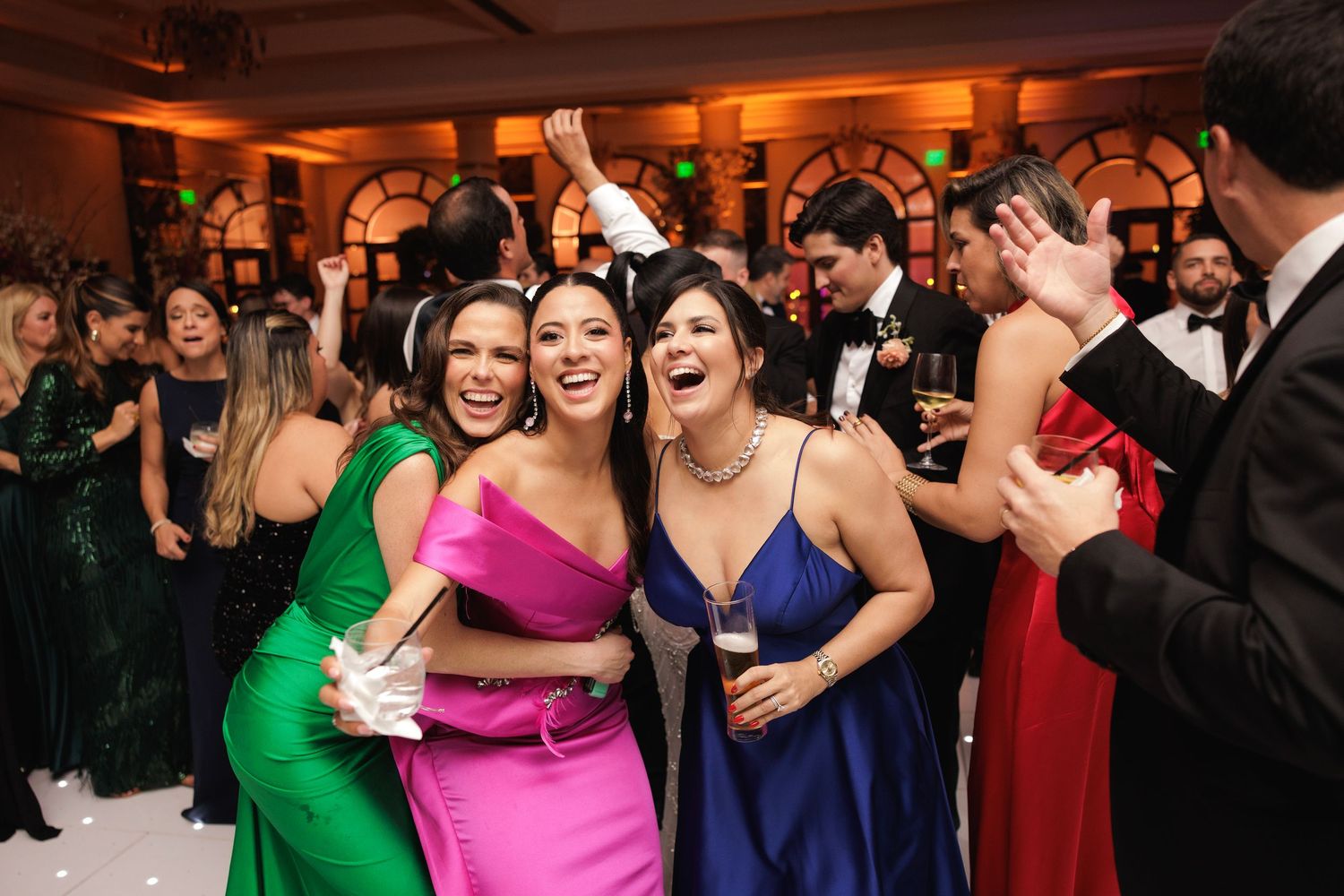 A group of wedding guests dance energetically together on the reception dance floor under warm lighting.