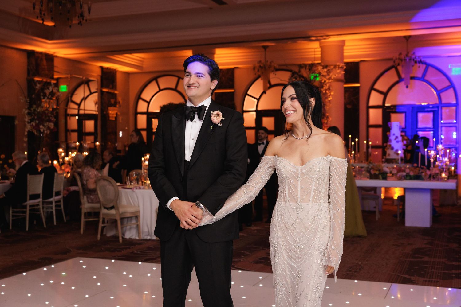 A couple shares a moment together on an elegant dance floor with warm lighting and decorative arches in the background.