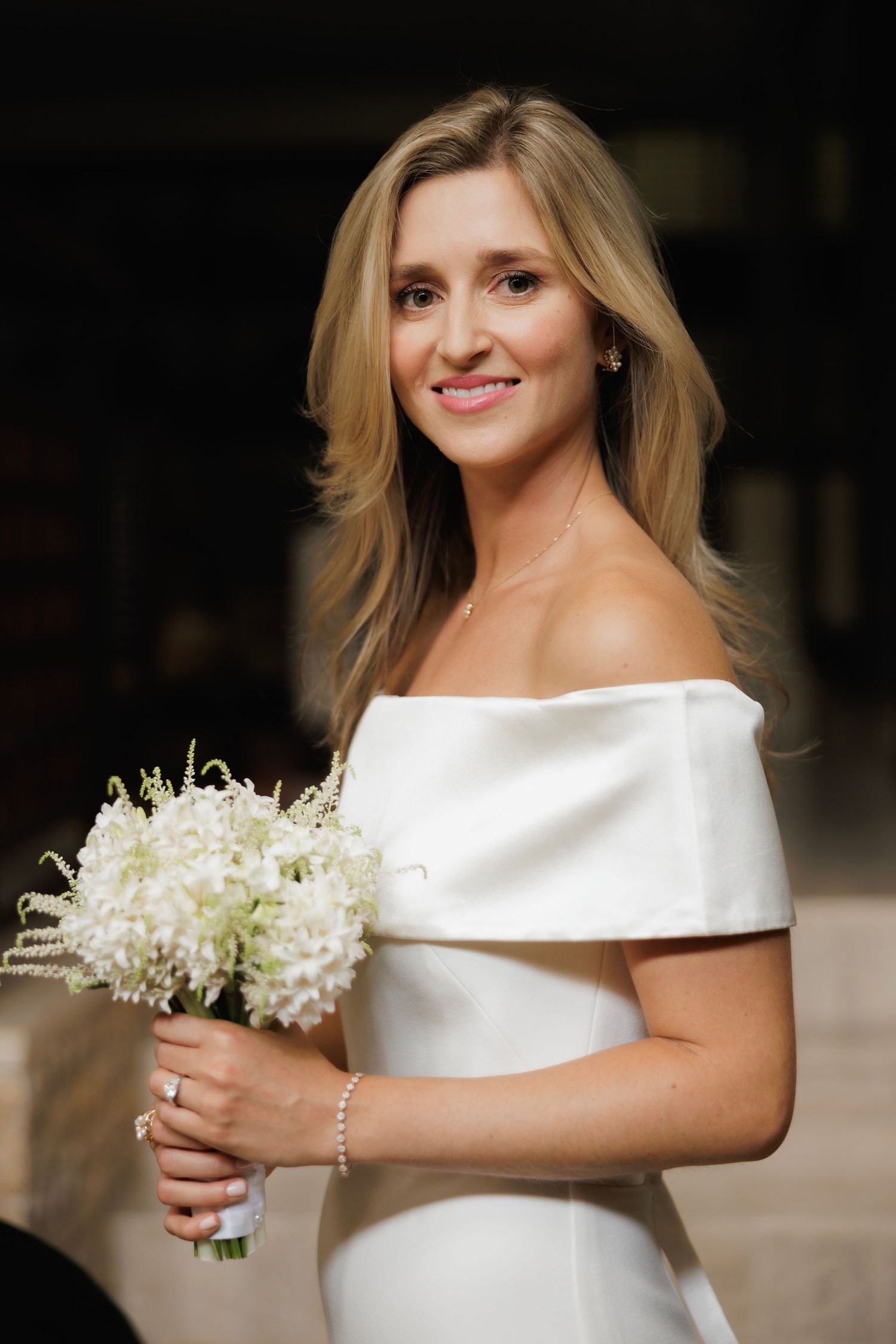 A bride in an elegant white off-shoulder wedding dress holds a delicate bouquet of lily of the valley flowers.