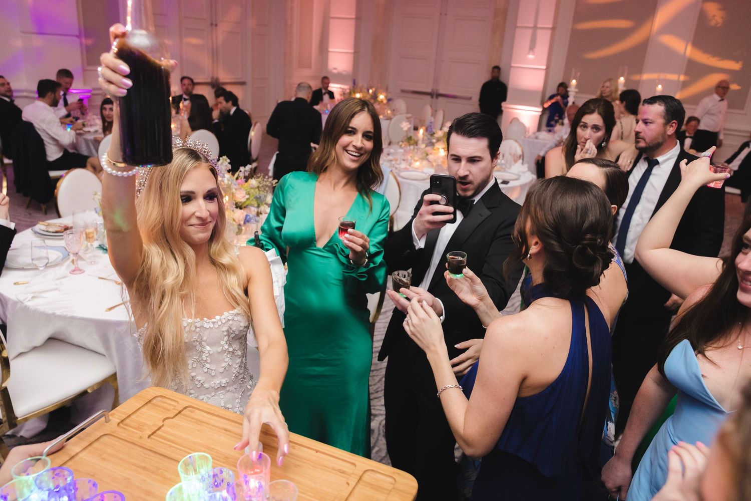 Party guests gather around a table at an elegant wedding reception with colorful lighting and decor.