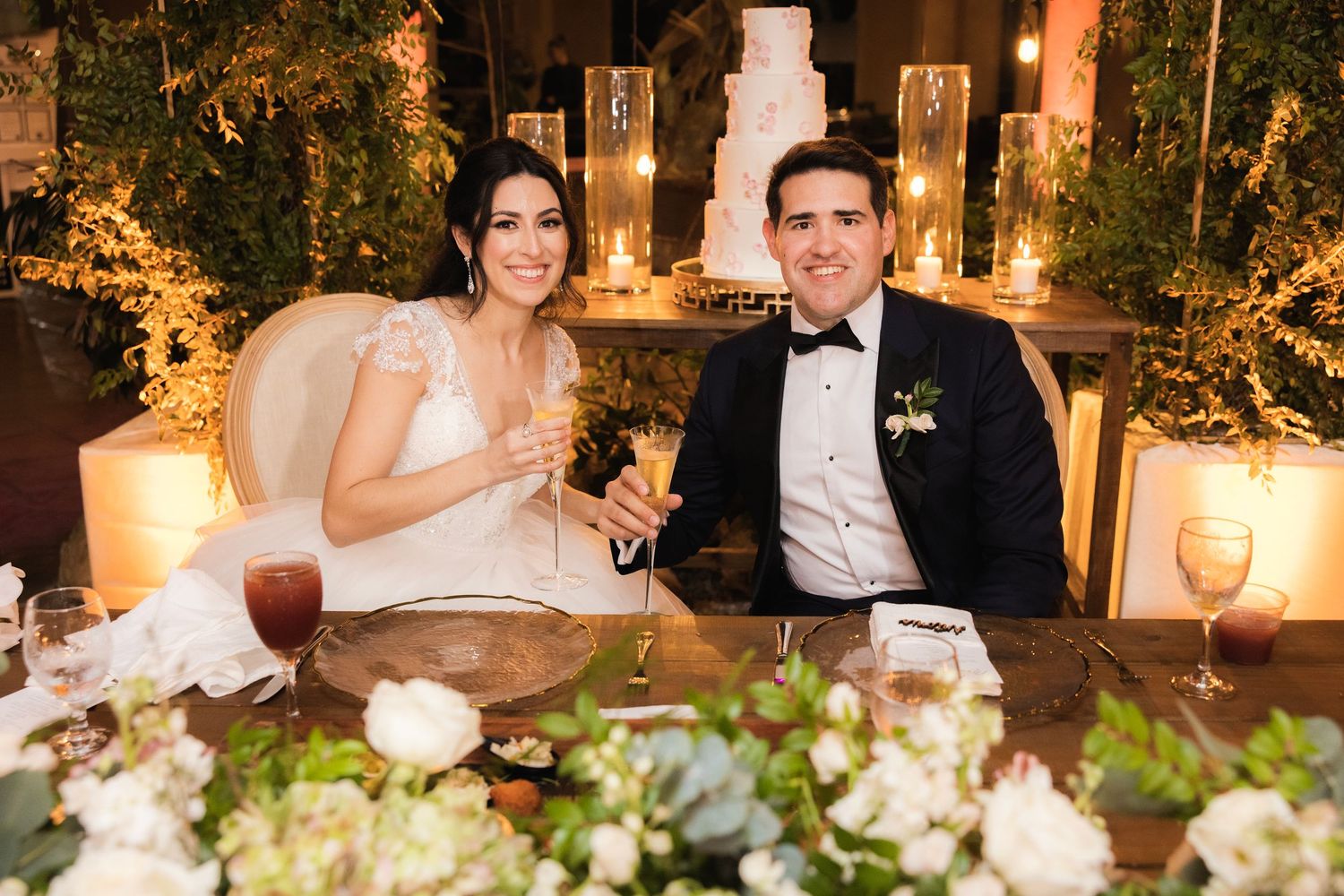 A beautiful wedding reception dinner table decorated with floral arrangements and warm candlelight at an evening celebration.