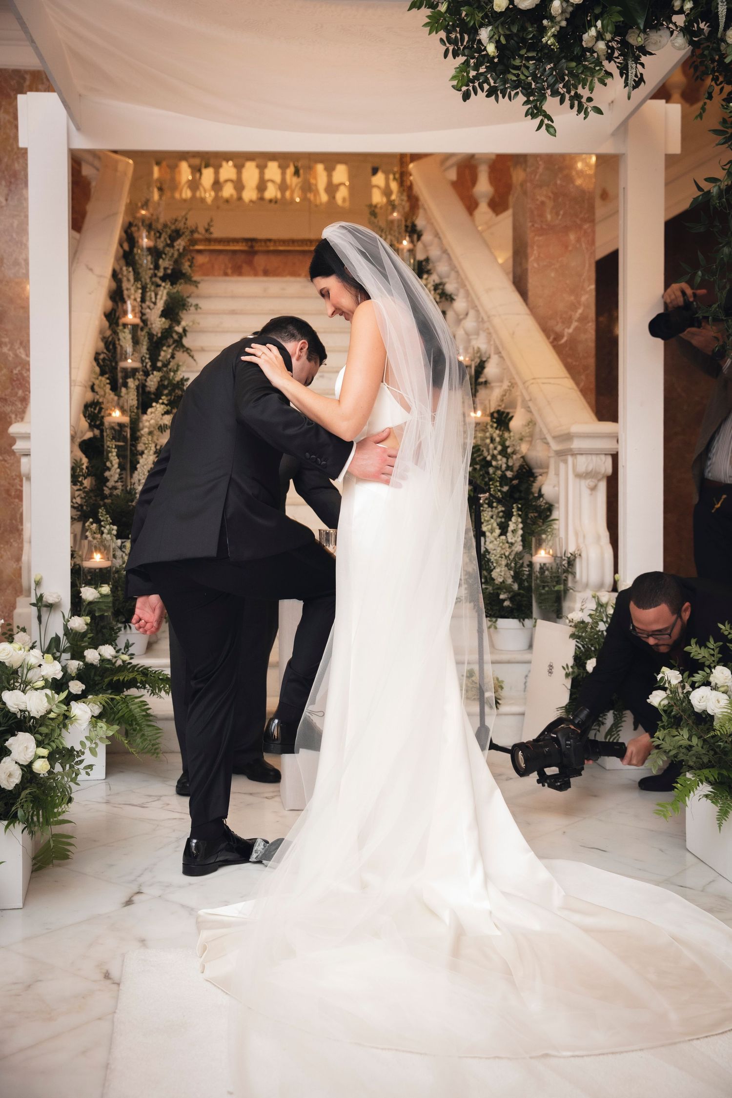 A romantic wedding ceremony setup with white floral arrangements and pillars in an elegant indoor venue.
