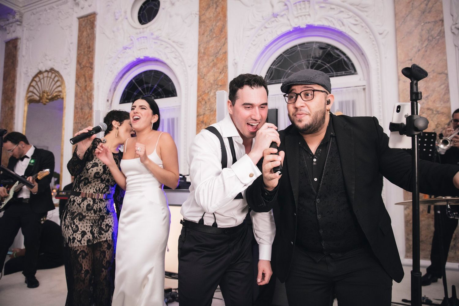 Wedding guests dance and celebrate together during a lively reception party with purple ambient lighting and ornate decor.