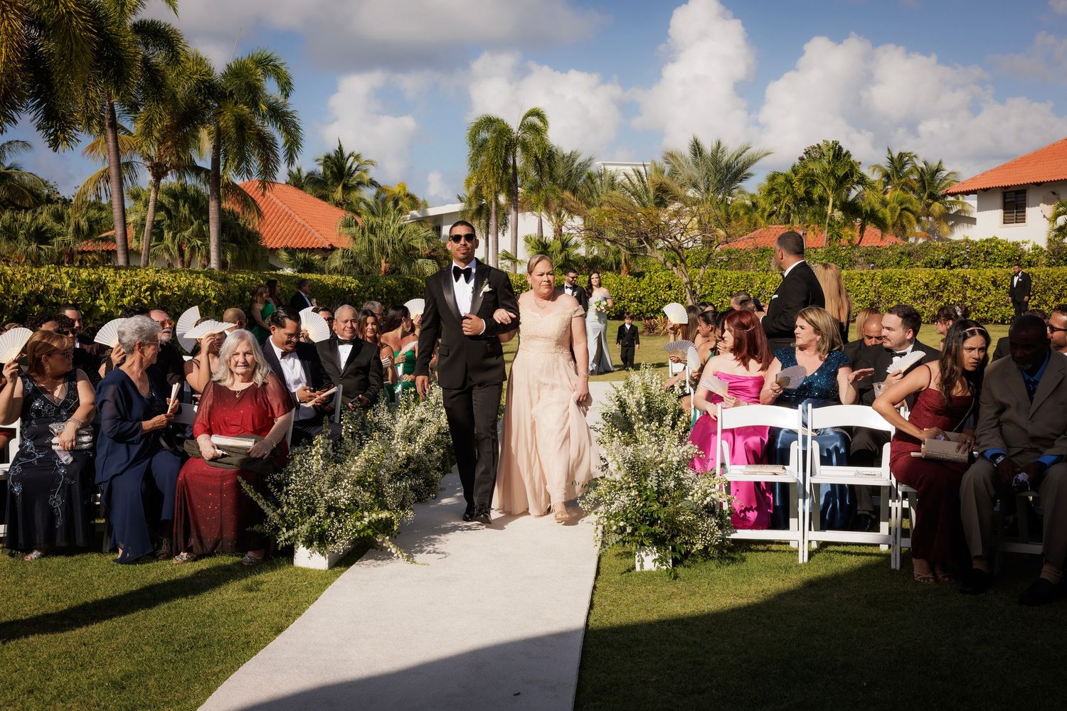 A scenic palm tree lined outdoor wedding ceremony venue in Florida with guests seated on either side of an aisle.