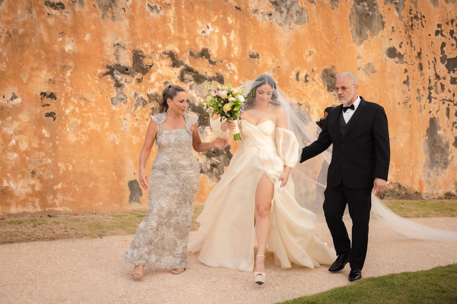 Wedding party posed against textured orange walls in warm afternoon light.