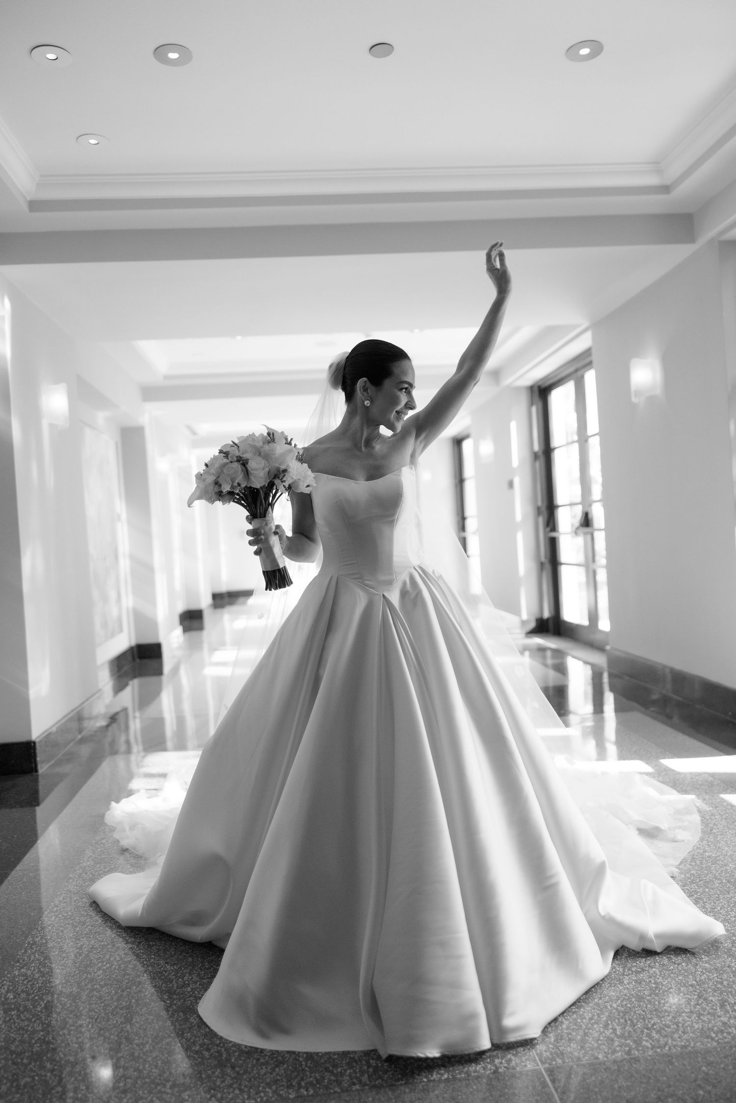 Bride in voluminous white ball gown twirling in bright hallway.