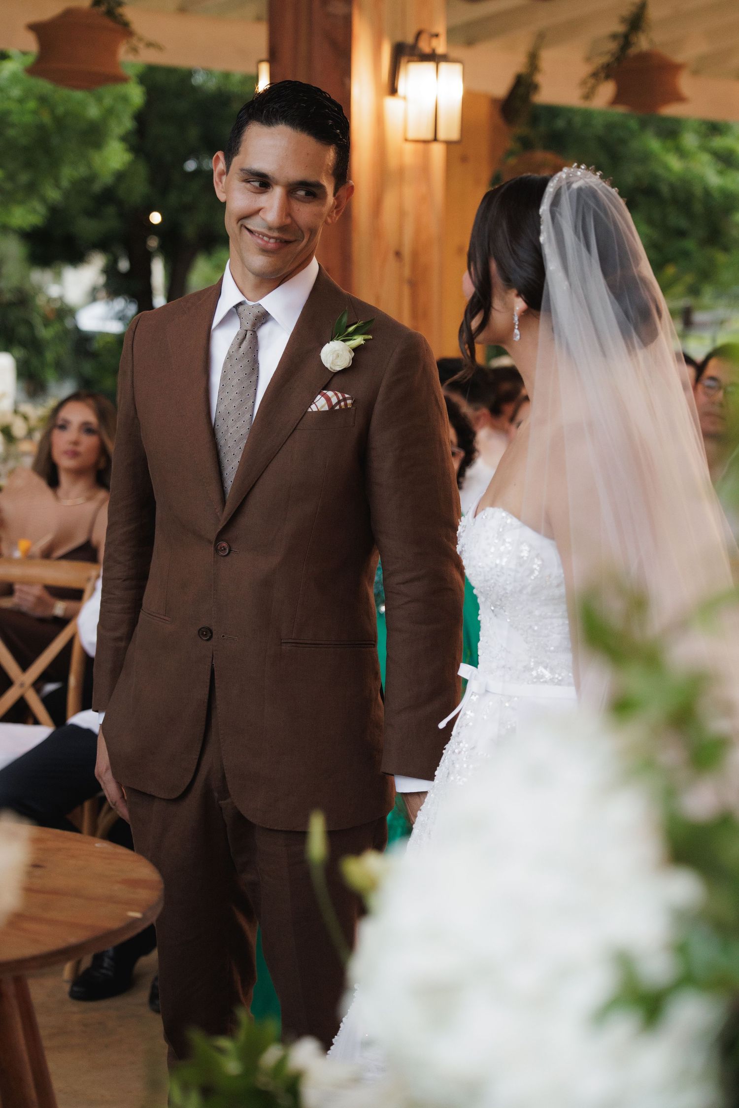 A wedding couple shares a joyful moment at an elegant venue with warm lighting and brown and white attire.