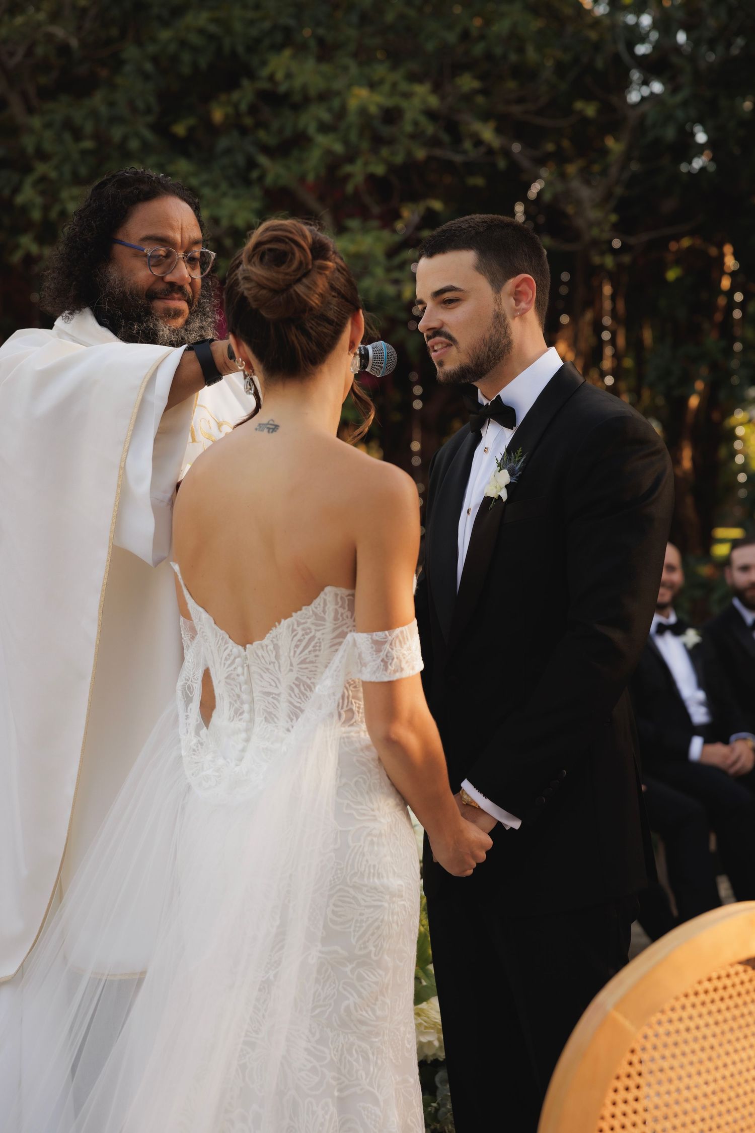 An outdoor wedding ceremony with the couple and officiant standing among greenery and white curtains.