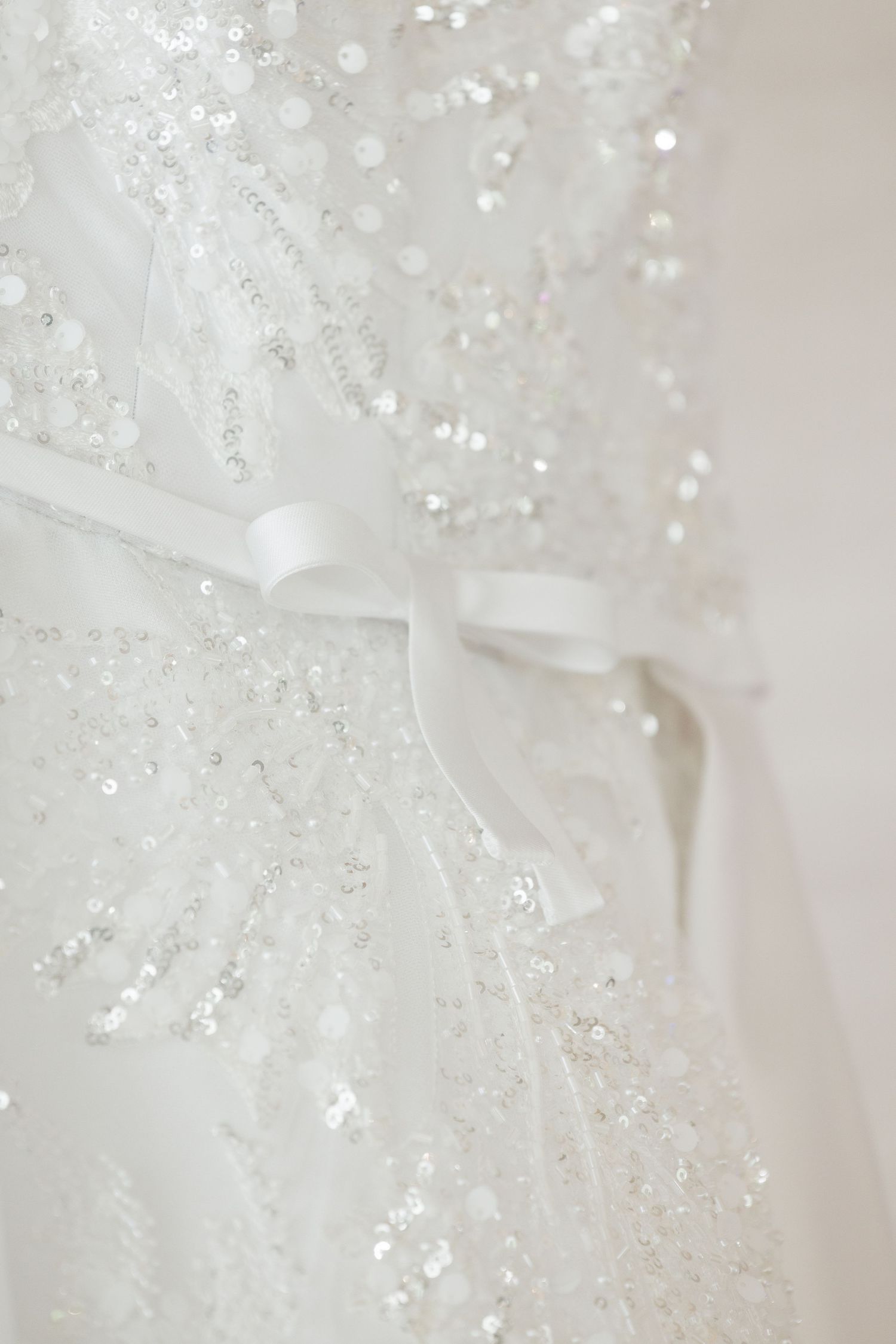 Close-up detail of delicate beading and ribbon on white wedding dress fabric.