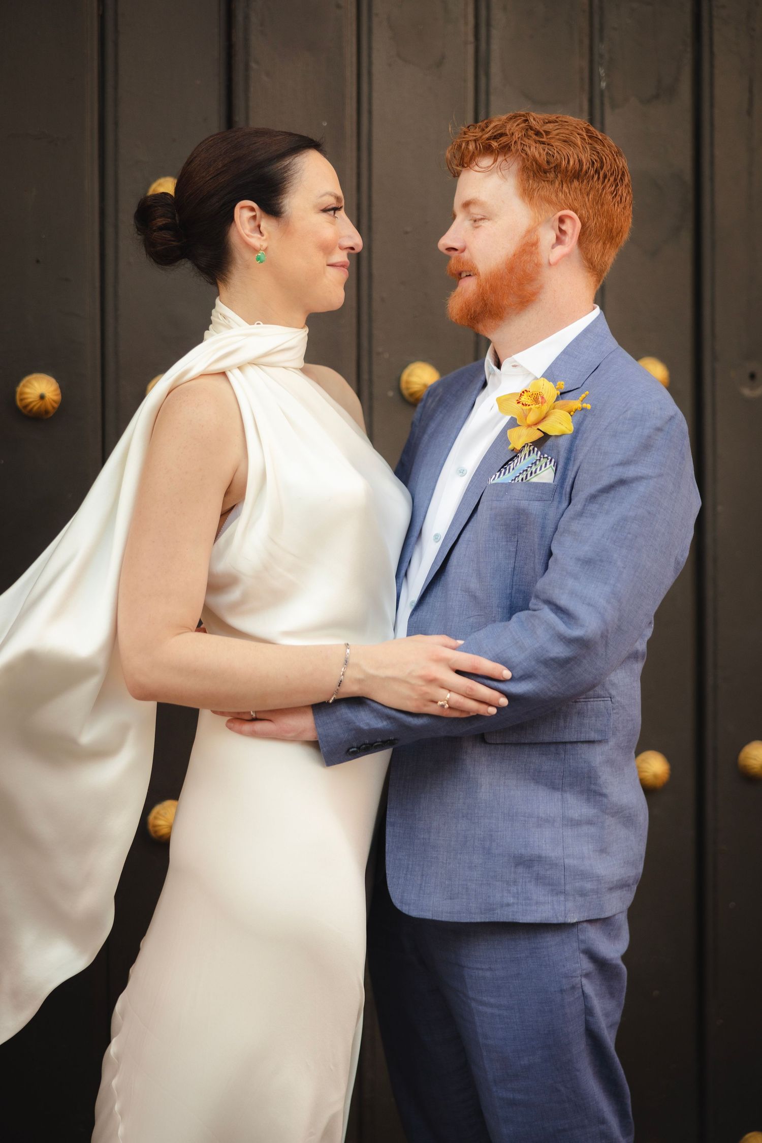A tender moment captured against dark wooden doors with brass fixtures.