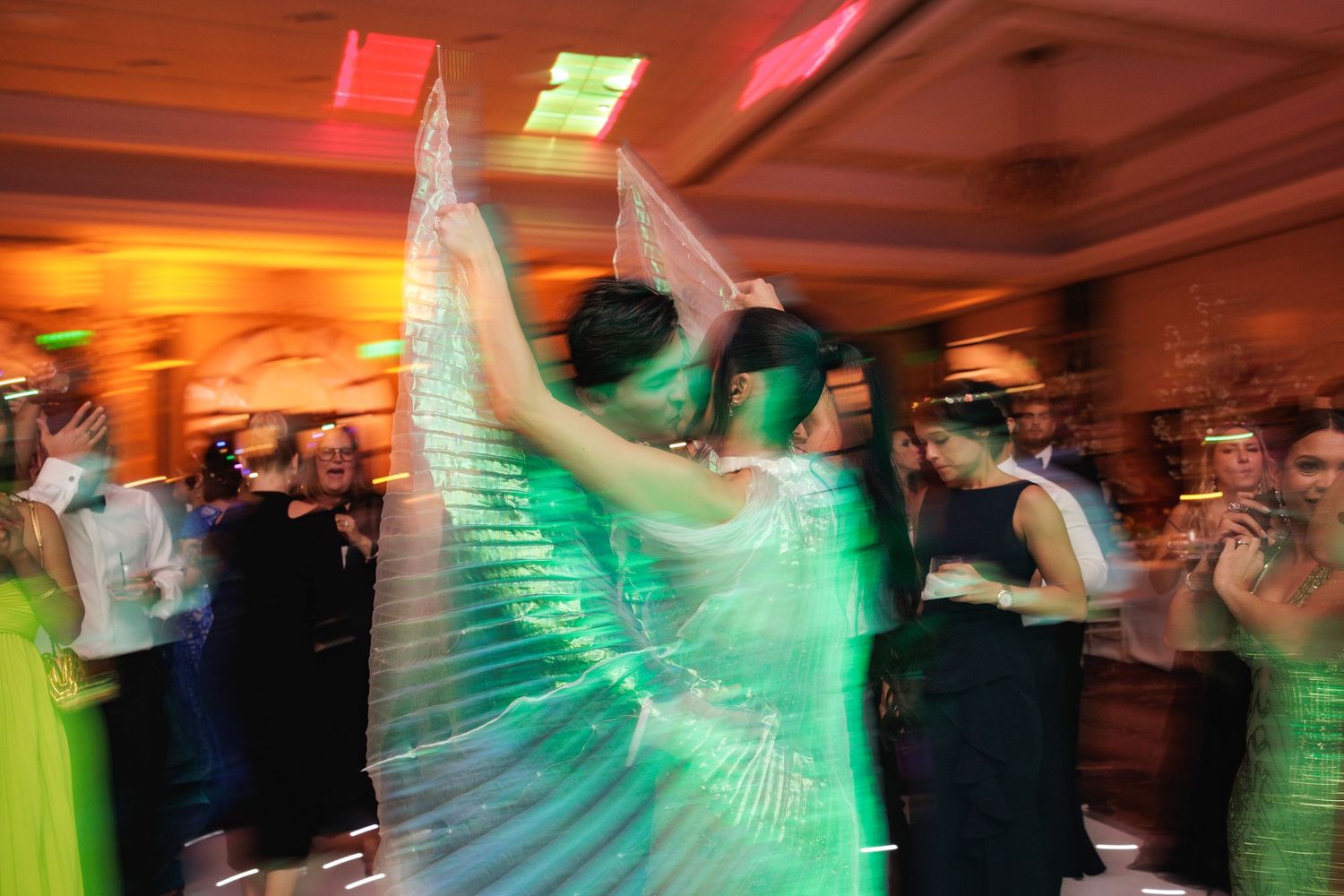 Wedding dance floor filled with motion-blurred guests in vibrant green and red lighting effects.