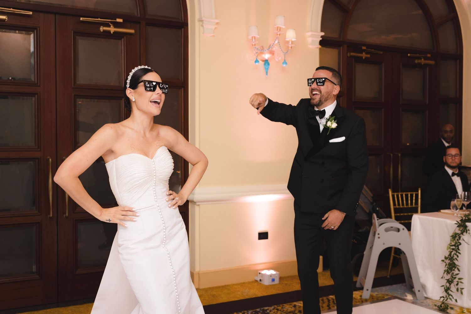 A joyful moment at a wedding reception as a couple strikes playful poses in formal attire.