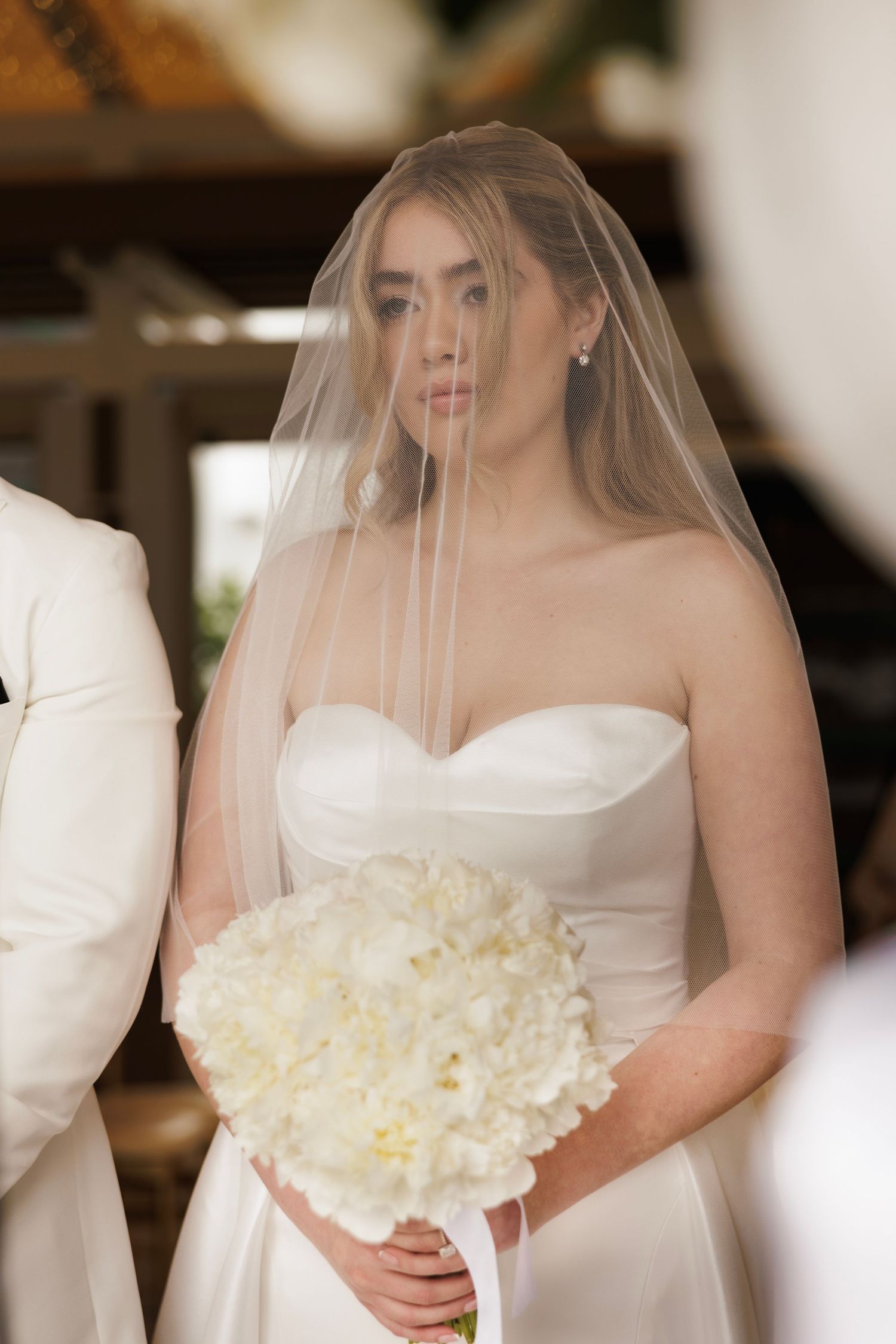 Wedding ceremony with bride in white dress holding bouquet of white peonies.