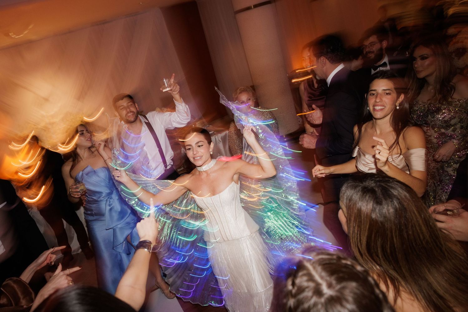 Lively wedding reception with dancers and guests surrounded by colorful light effects.