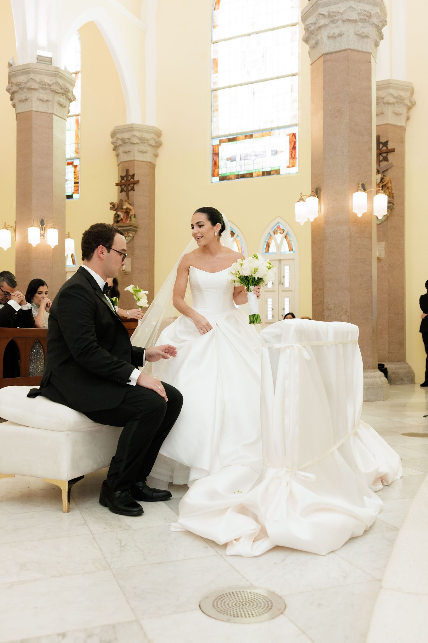 Wedding couple seated during church ceremony surrounded by elegant architecture.