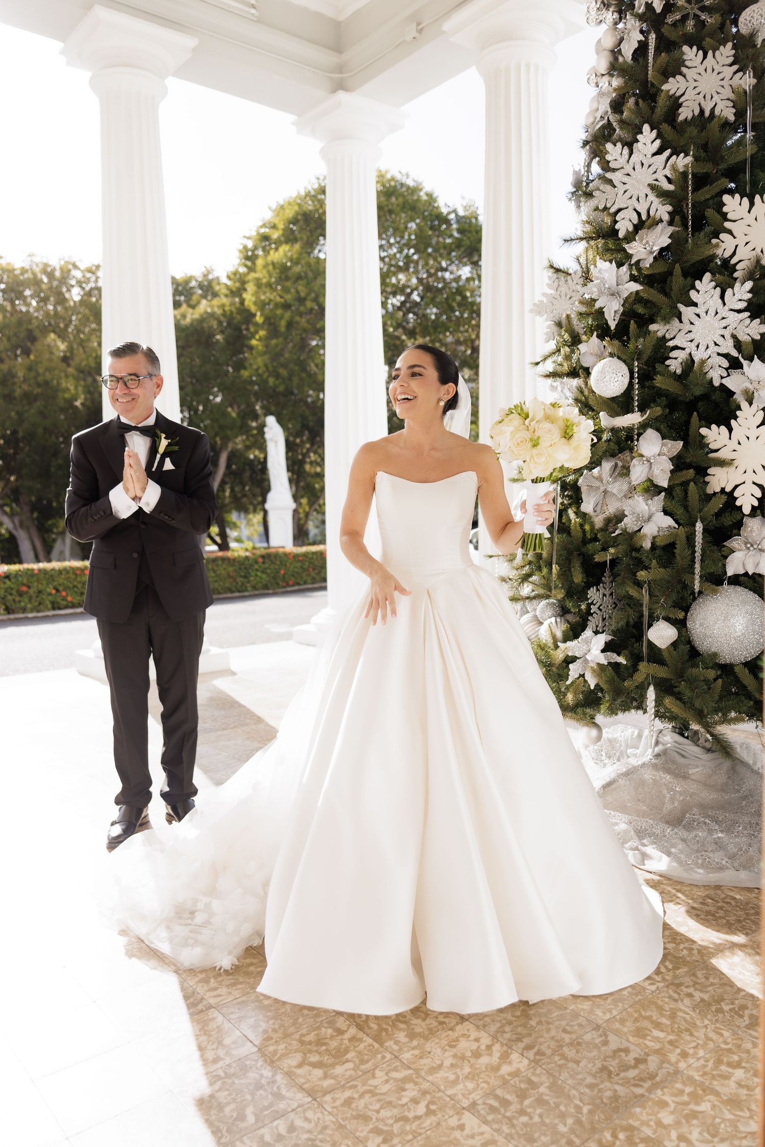 Playful wedding couple poses together in a white gazebo decorated with elegant white floral arrangements.