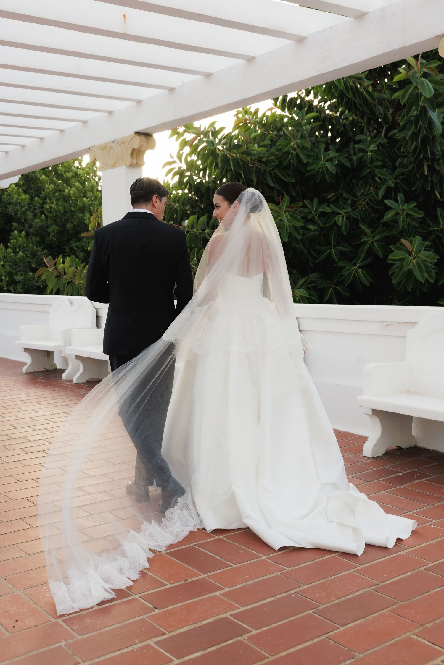 A couple twirls on an outdoor terrace with white pillars and terracotta tiles.