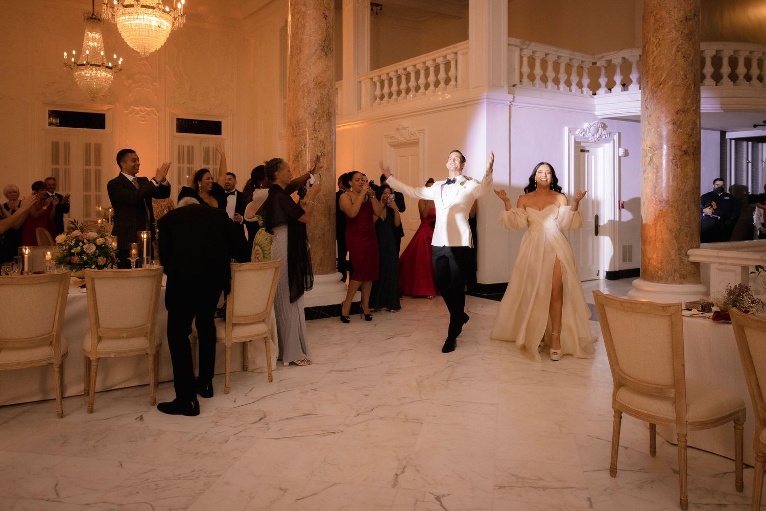 Couples learning ballroom dance steps in an elegant studio with ornate columns and chandeliers.