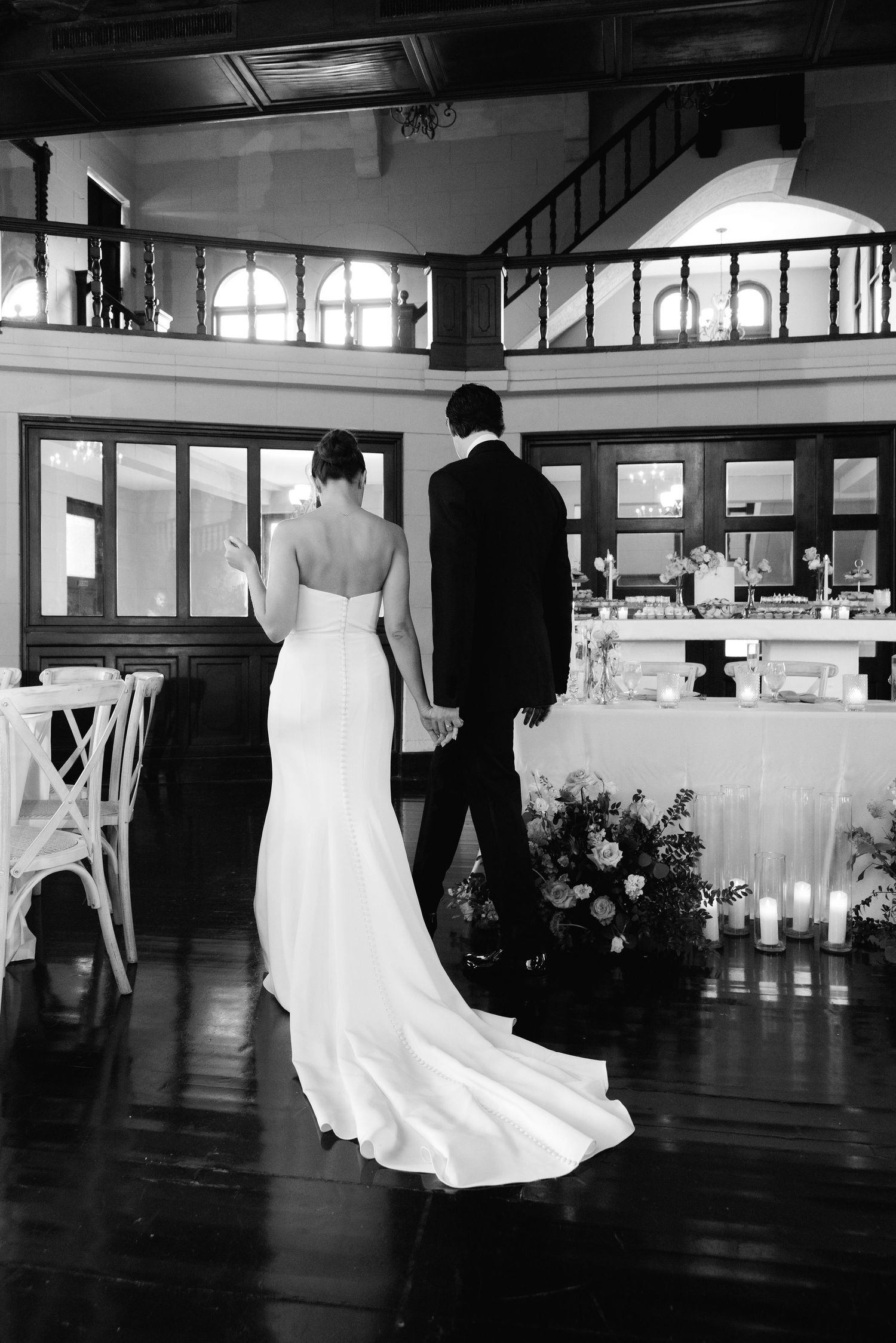Black and white panoramic view of a wedding reception showing dancing silhouettes on a dark hardwood floor.