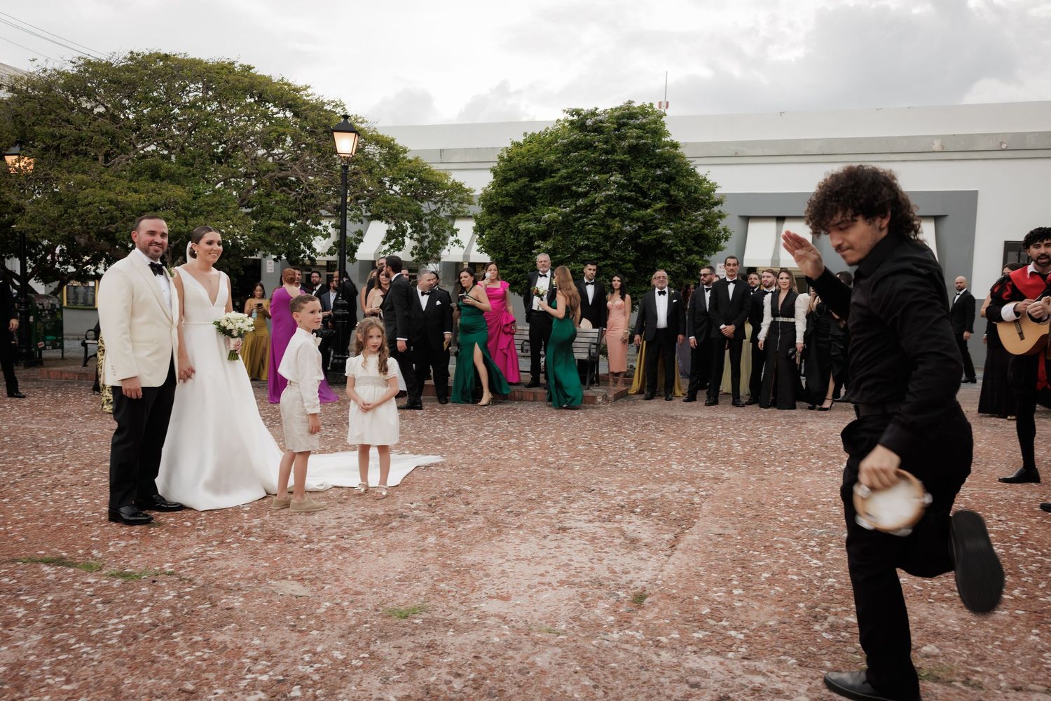 Wedding guests gather on a pink cobblestone courtyard during an outdoor reception celebration.