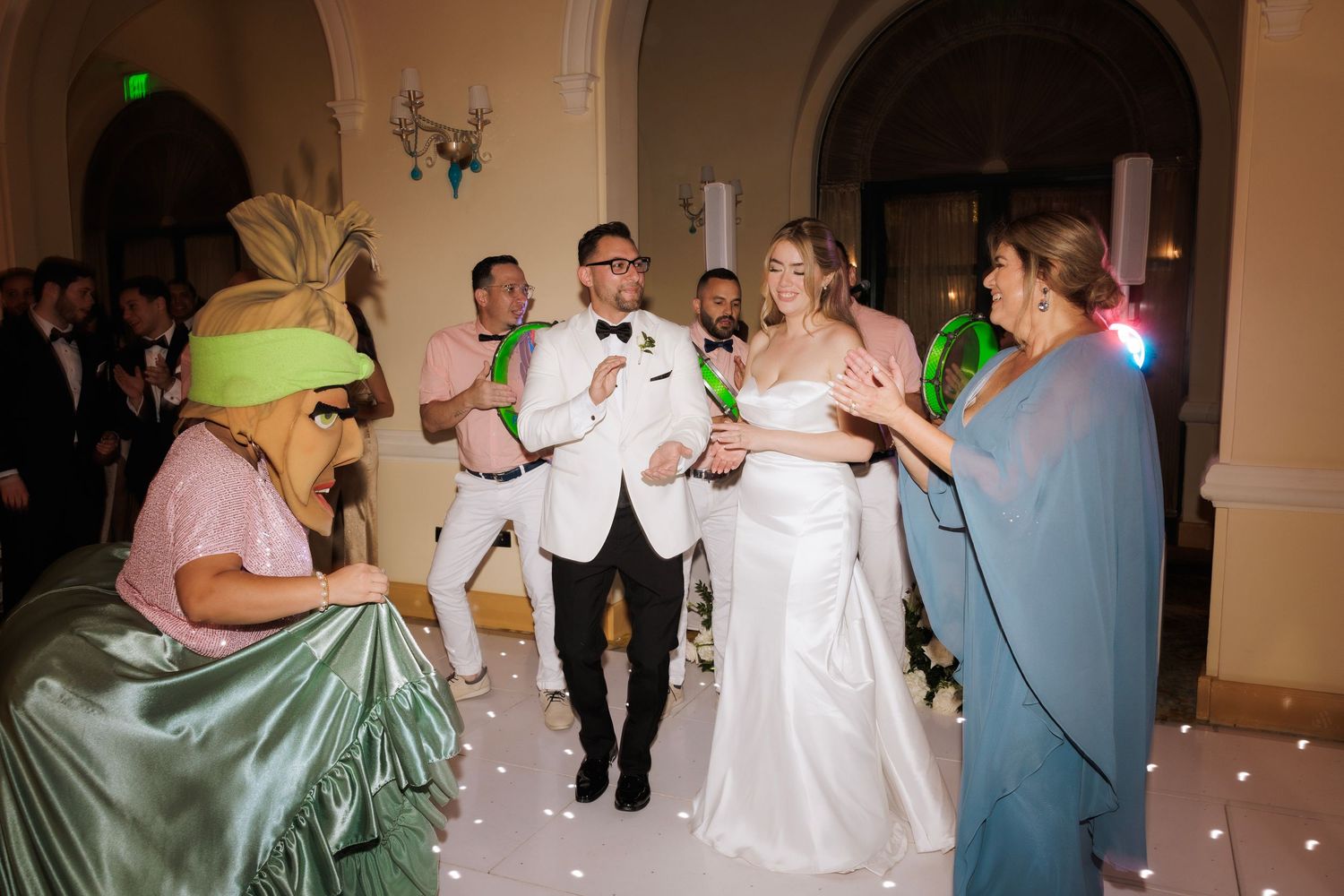Wedding celebration with guests dancing and mingling in a grand ballroom with arched architecture.