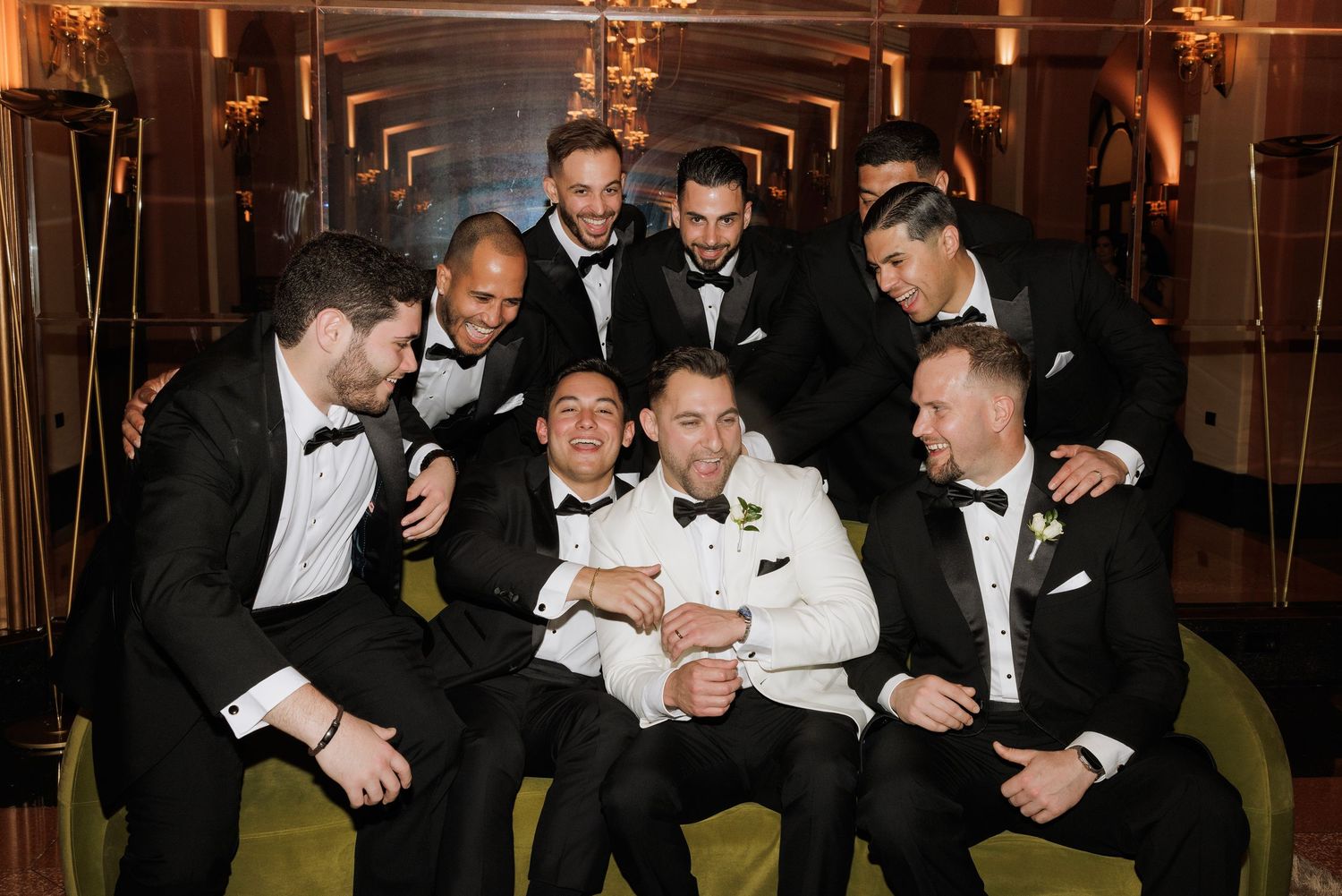 A group in black tuxedos gather closely together for a celebratory moment at an elegant venue.