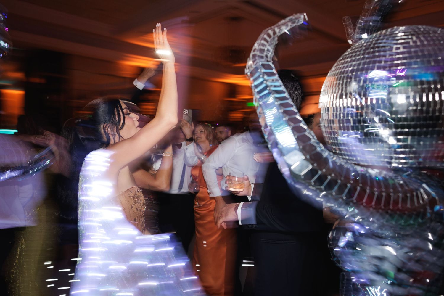 A disco ball reflects light on a crowded dance floor at a wedding celebration.