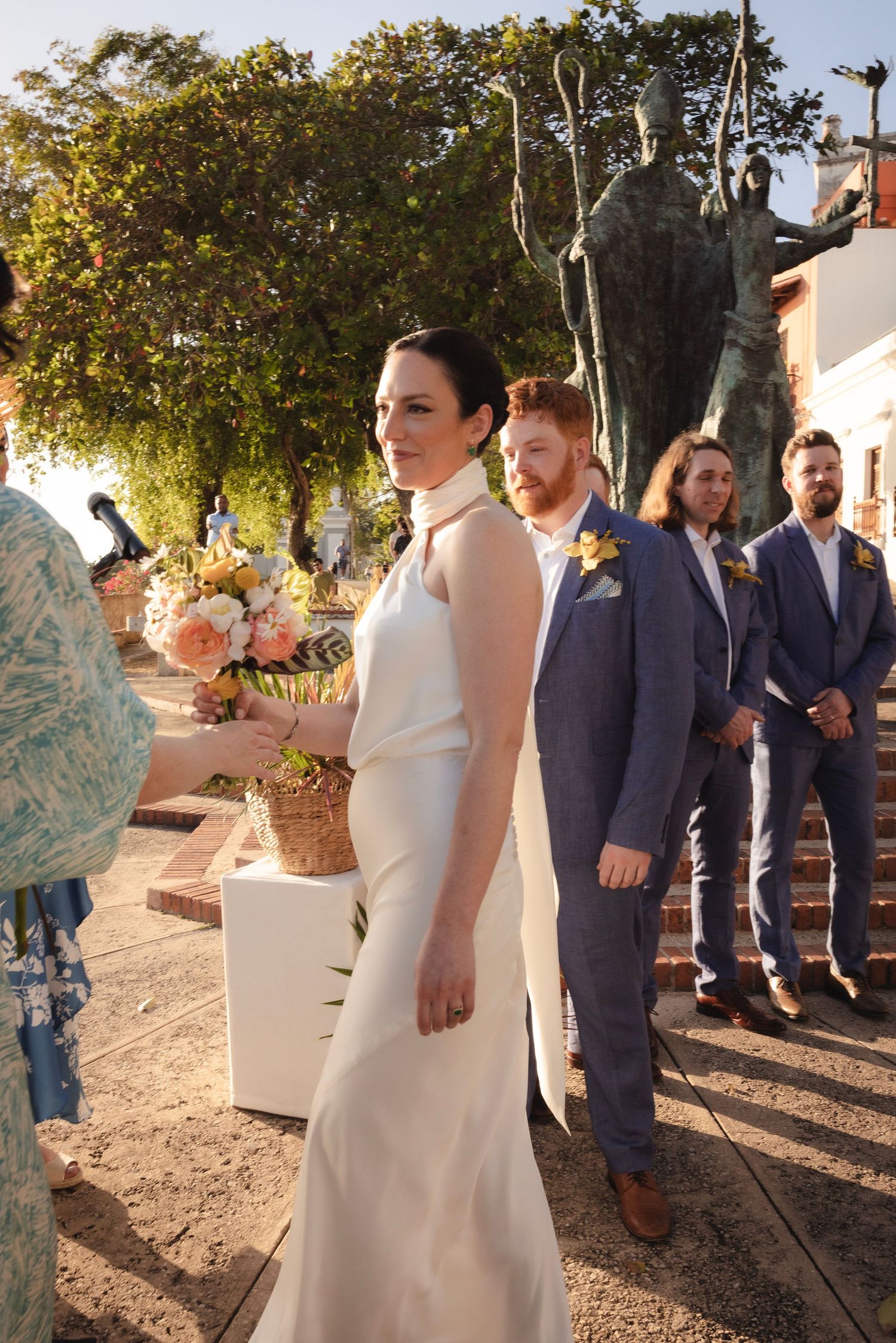 Wedding party members in navy suits and white dresses lined up outdoors at sunset.