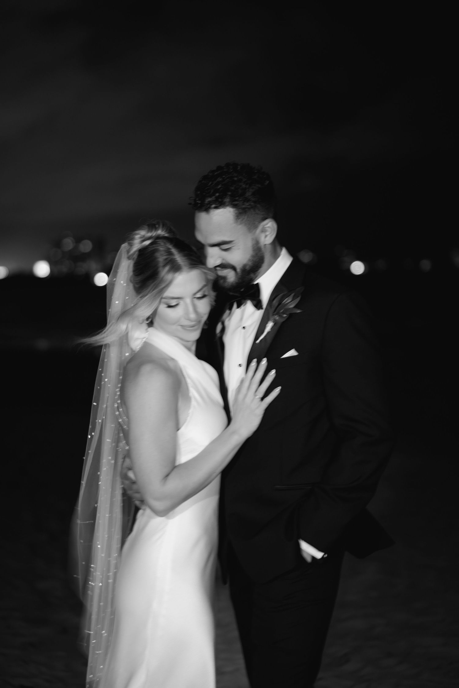 An intimate black and white nighttime portrait of newlyweds sharing a tender moment.