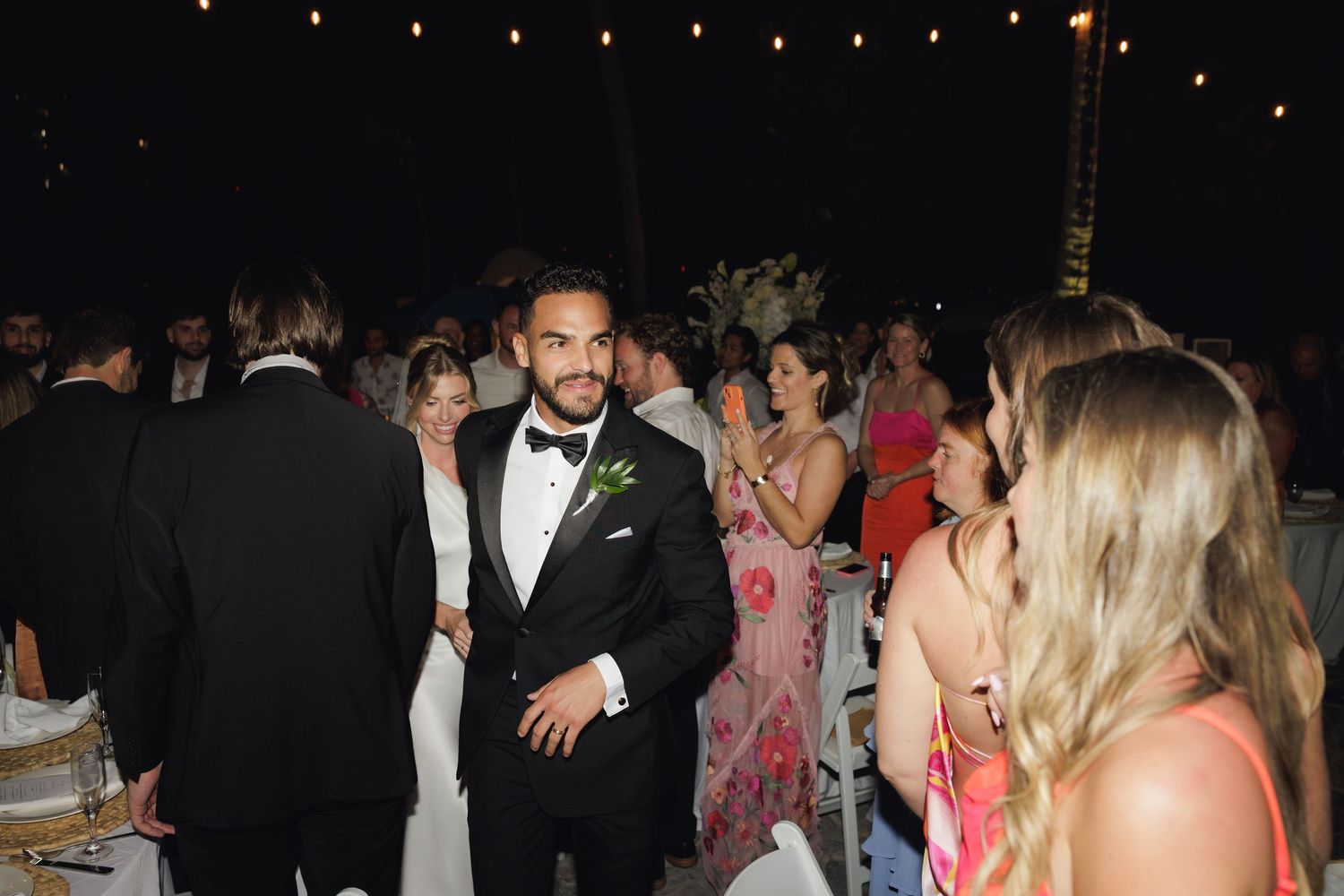 Wedding guests enjoying a festive reception at night with string lights and formal attire.