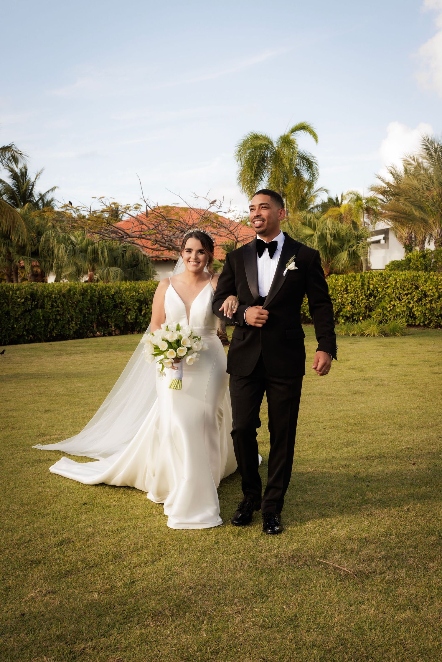 Three photos of wedding couple walking together across a sunny lawn with palm trees in the background.