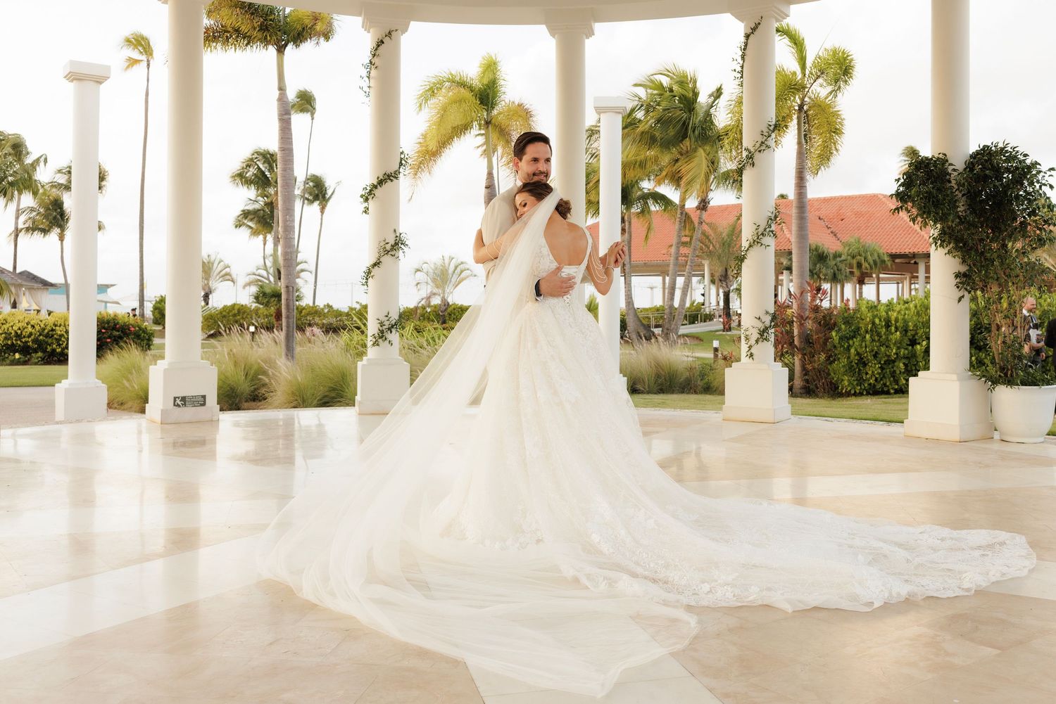 A row of wedding dresses displayed under elegant white gazebos with palm trees in the background.
