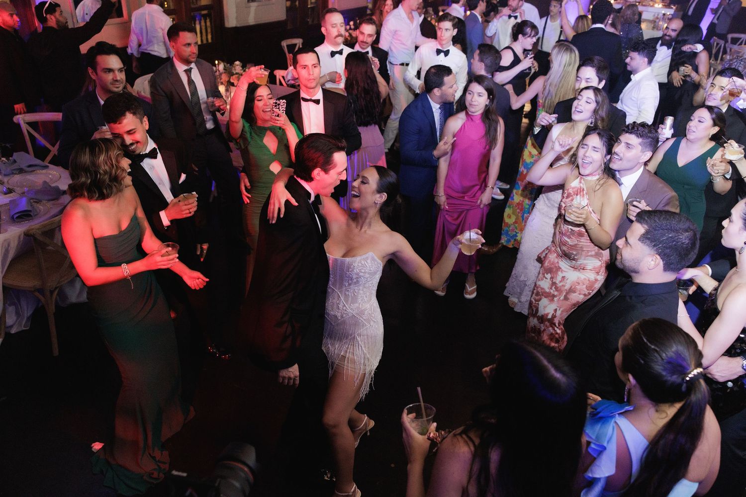 People dancing and enjoying themselves on a dark dance floor with colorful lighting at a nightclub party.
