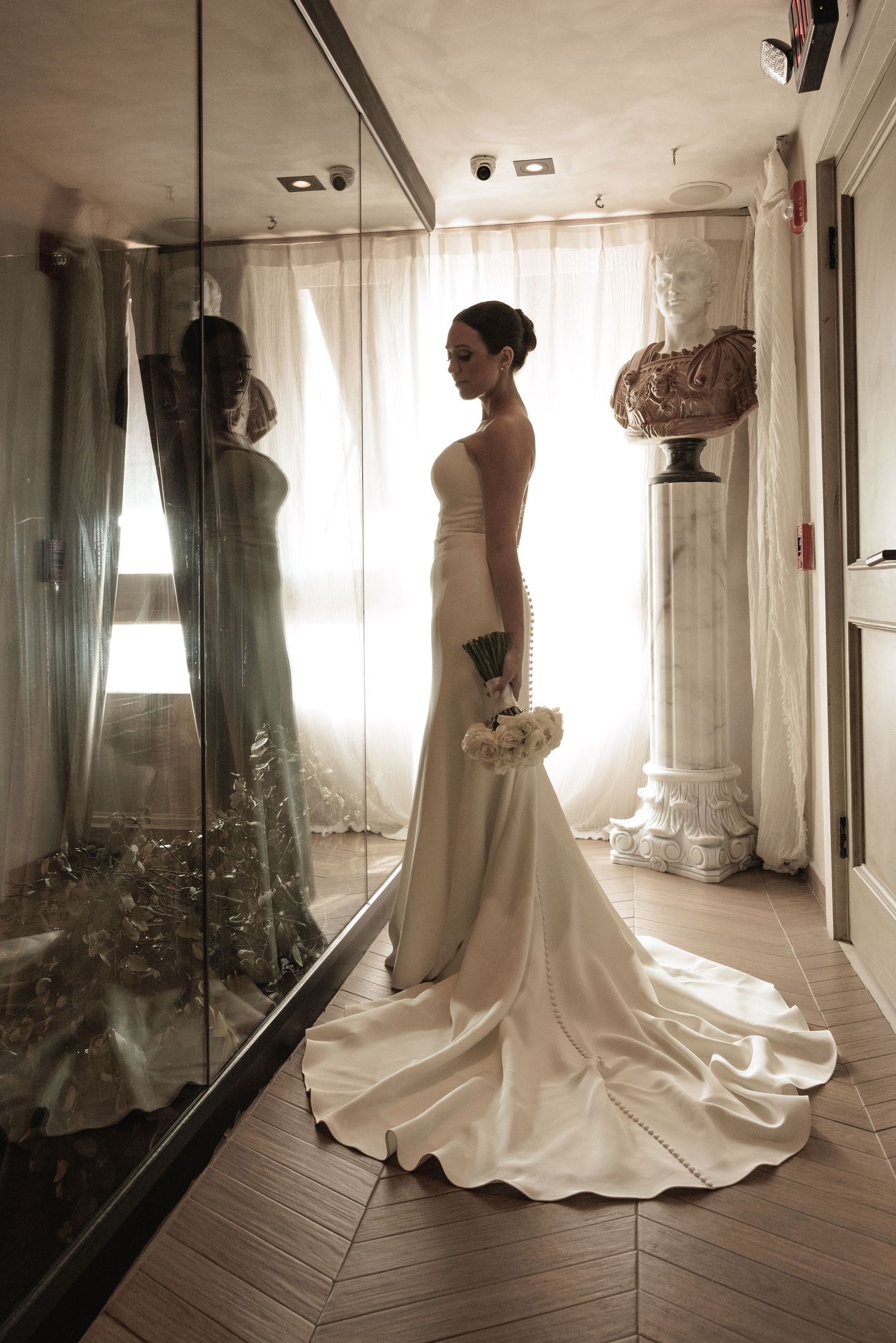 Elegant bridal gown with train captured in multiple mirror reflections in sunlit dressing room.