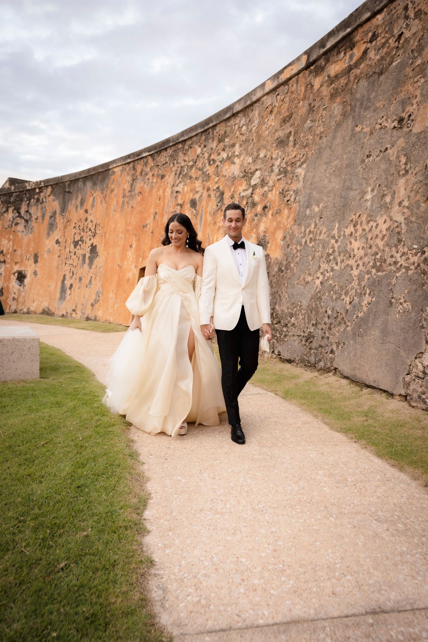 Wedding couple strolls along picturesque stone fortress path during their photo session.
