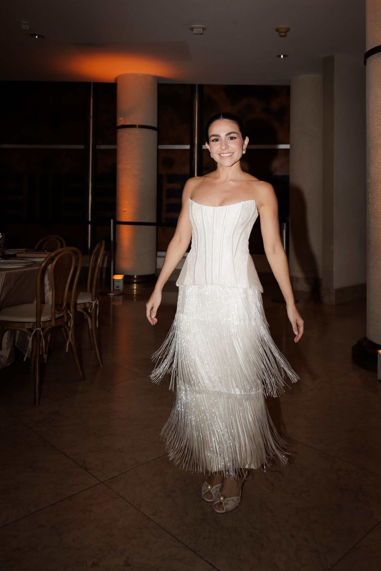 A dancer in a white fringed dress twirls and spins in a dimly lit venue.