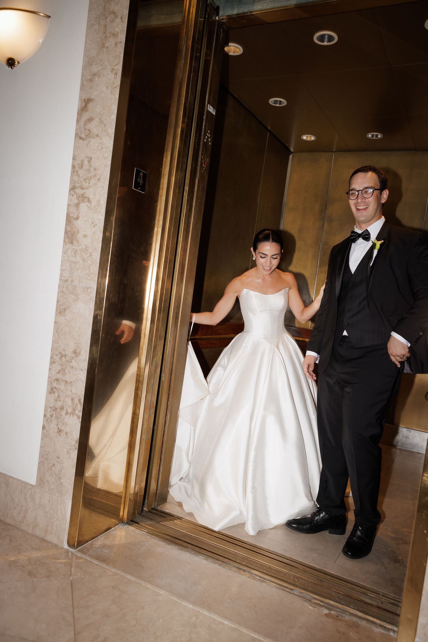 A bride in a white wedding gown and groom in black suit exit through a series of elevator doors in sequence.