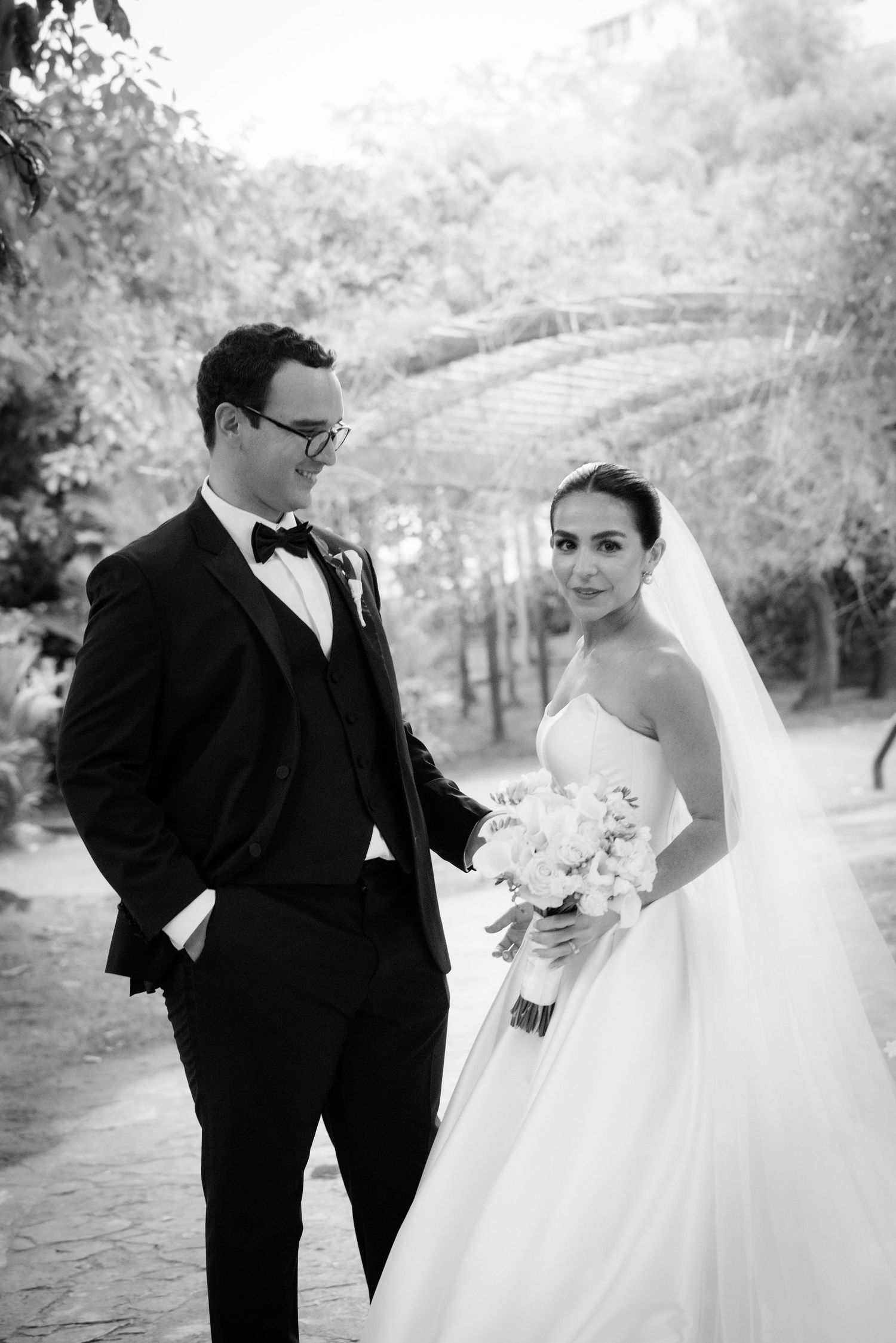 Black and white portrait of newlyweds on a tree-lined path.