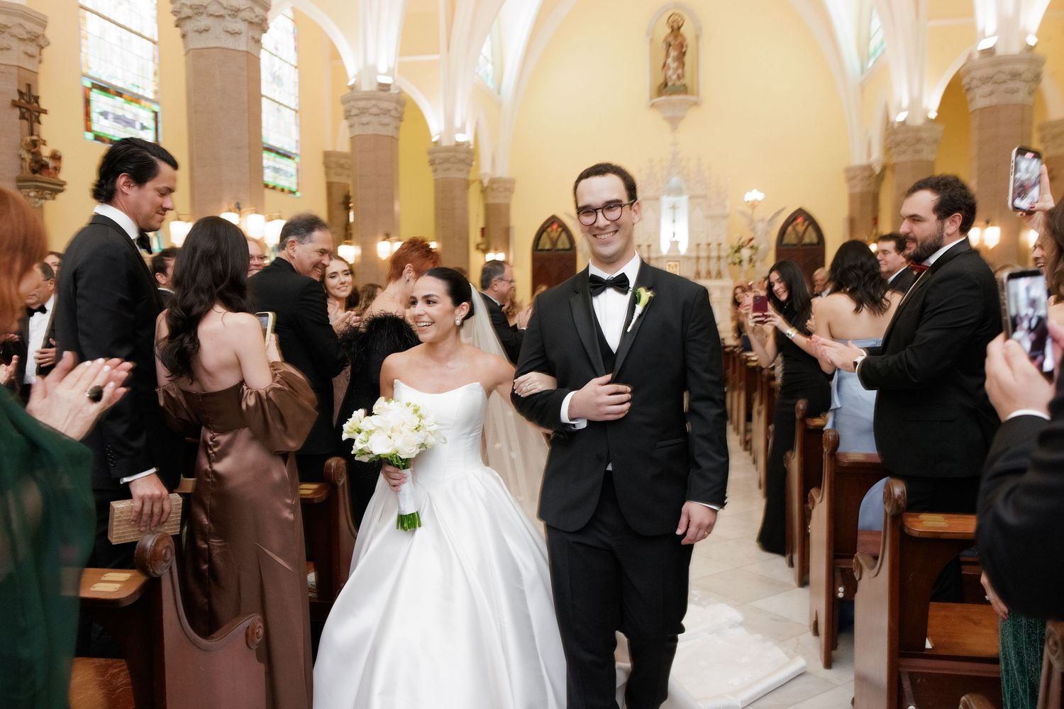 Wedding party celebrates inside a traditional church with arched columns and warm lighting.