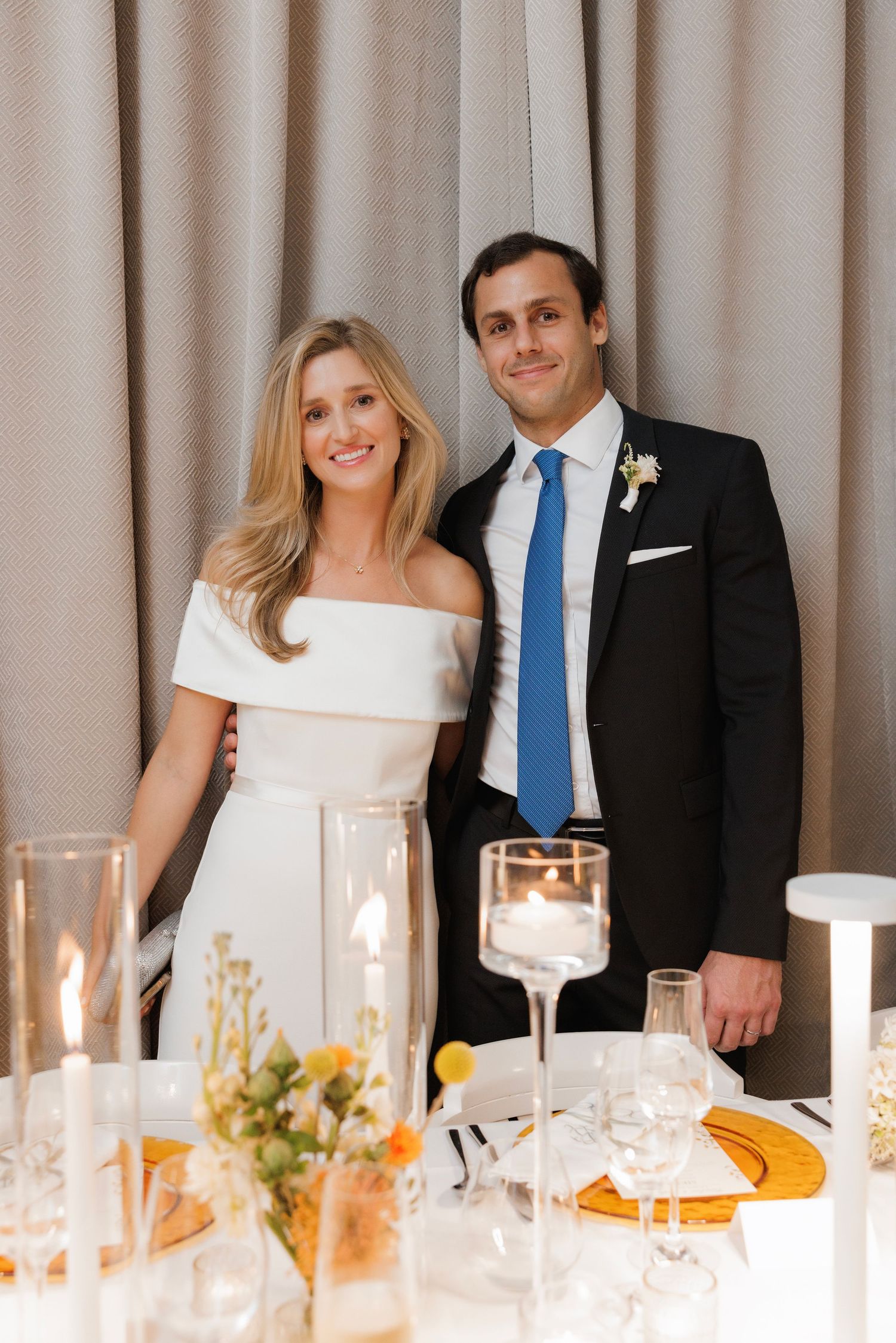 A couple poses at an elegant wedding reception with a table set with glowing candles and wine glasses.