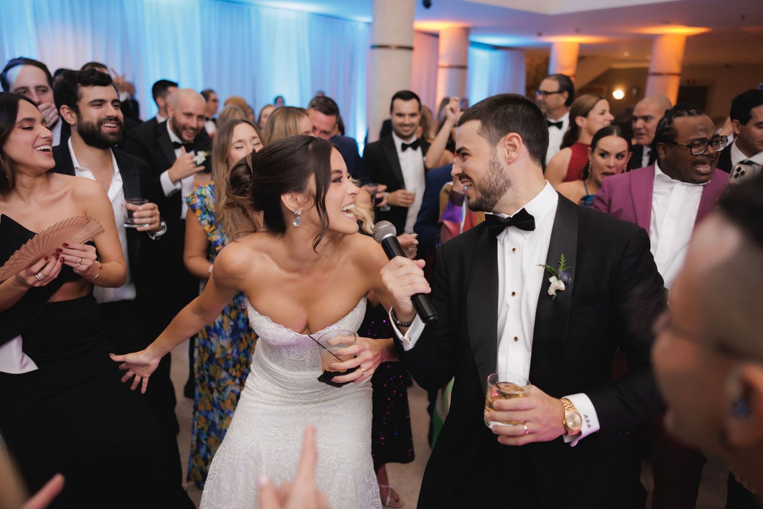 Happy newlyweds dance together surrounded by joyful wedding guests at their reception celebration.