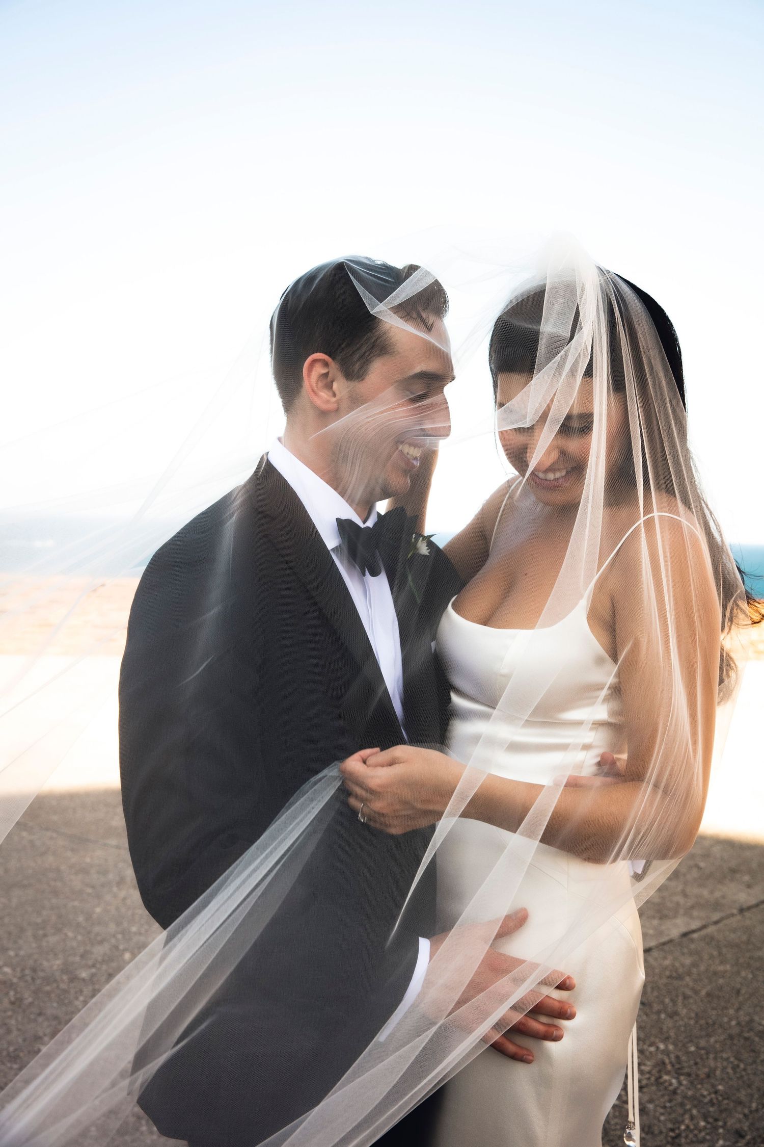 A romantic wedding portrait of a couple on the beach with the bride's veil flowing in the breeze.