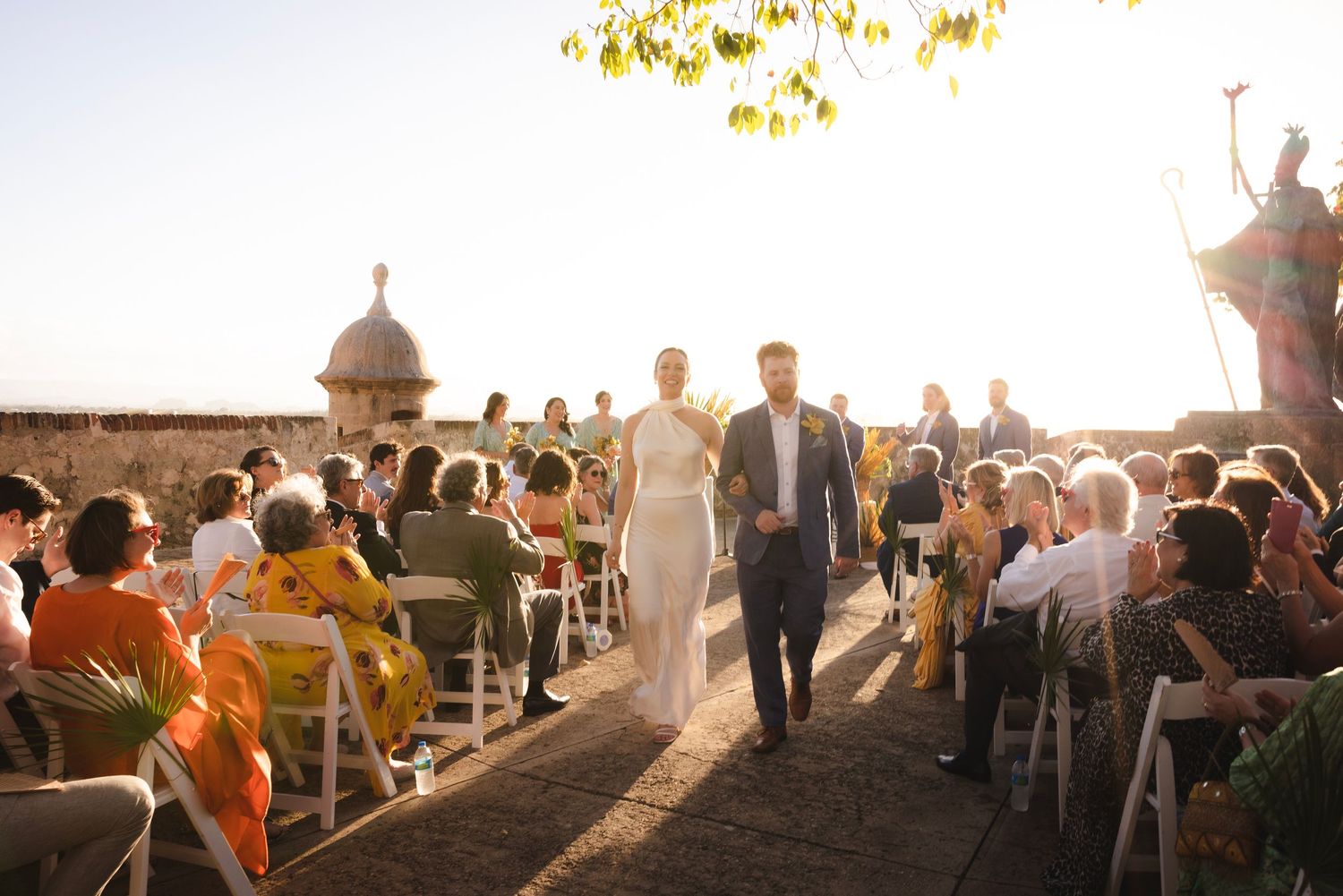 Wedding guests mingling outdoors during a golden sunset reception.