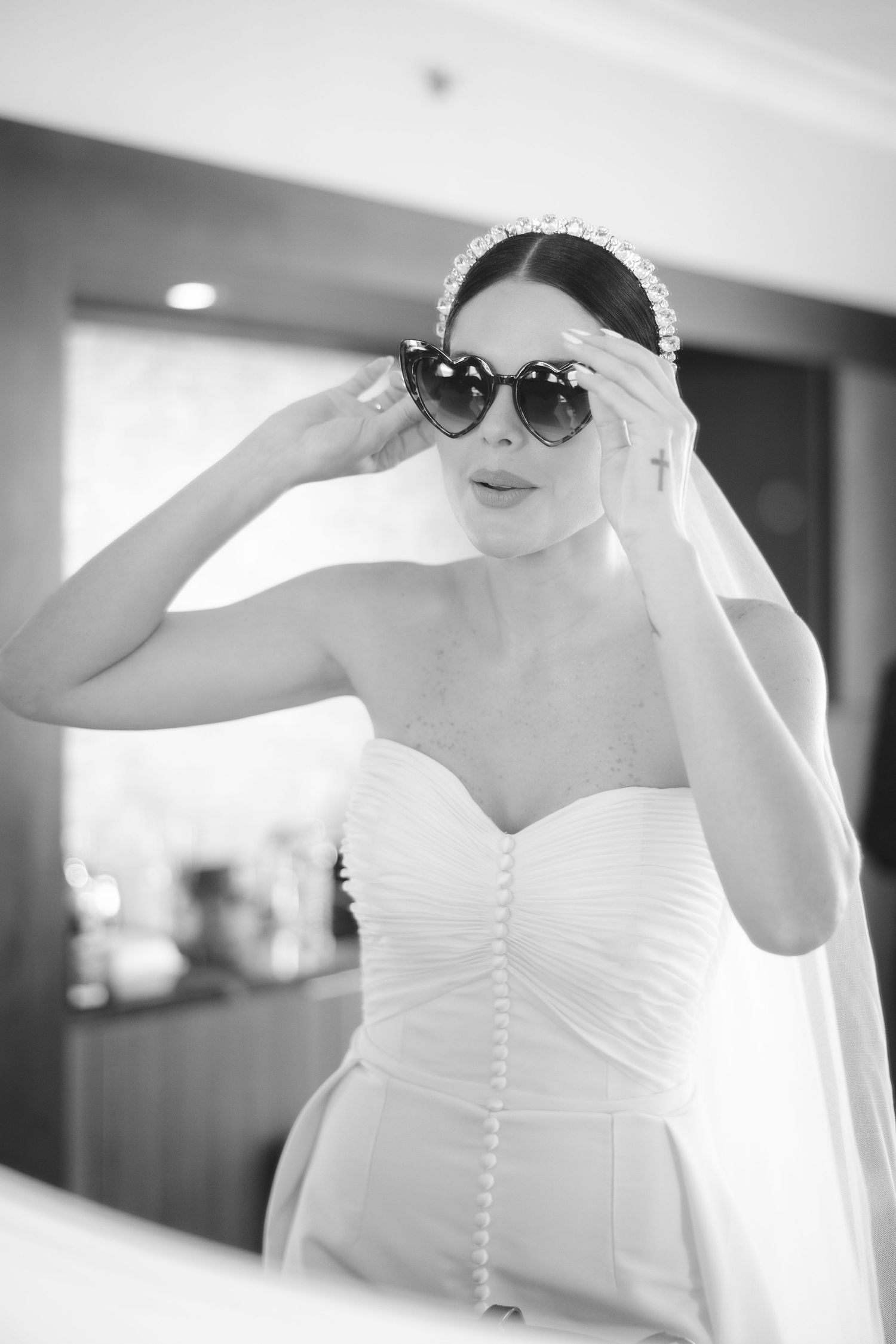 A bride wearing sunglasses and a wedding dress poses playfully in black and white.