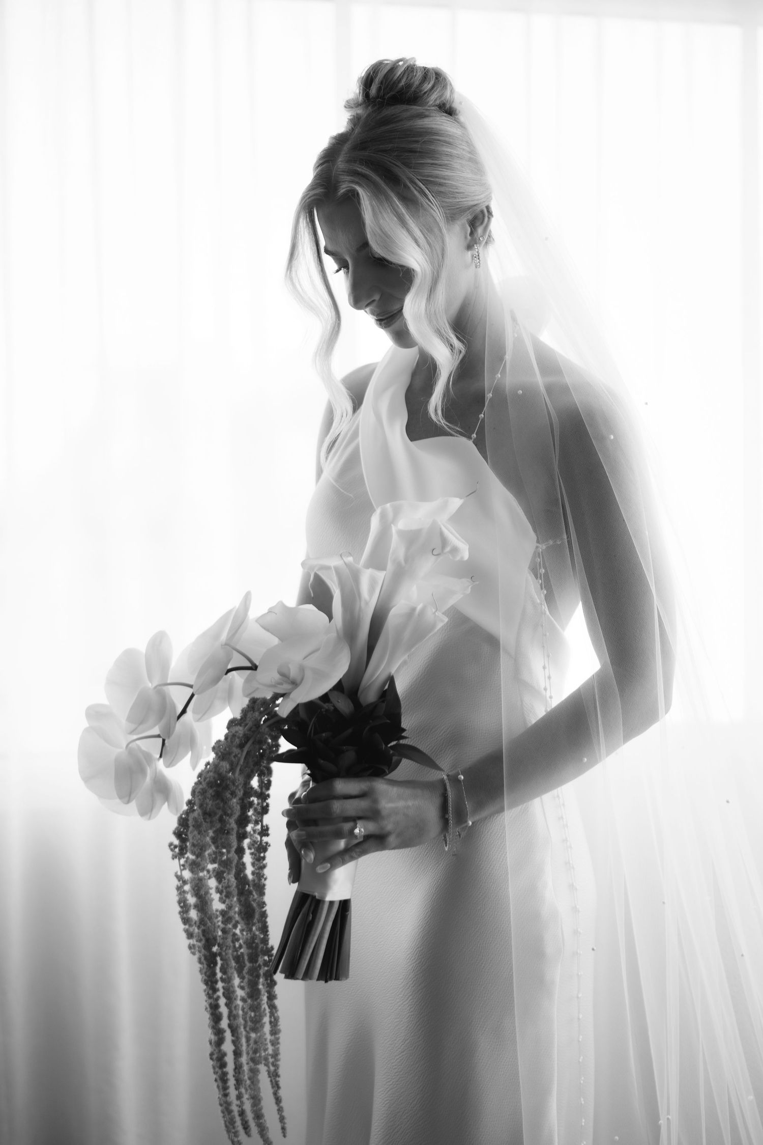 A romantic black and white bridal portrait with cascading bouquet and flowing veil in soft window light.
