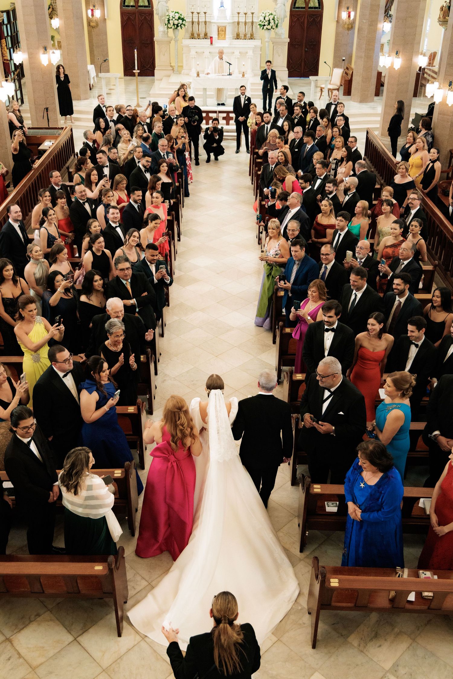 Overhead view of a church wedding ceremony with guests filling the pews and a bride walking down the center aisle.